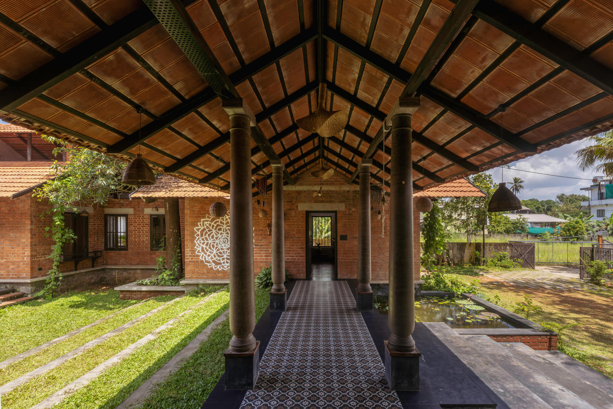 Covered walkway with steel columns and timber ceiling beams overlooking the stepped grass courtyard