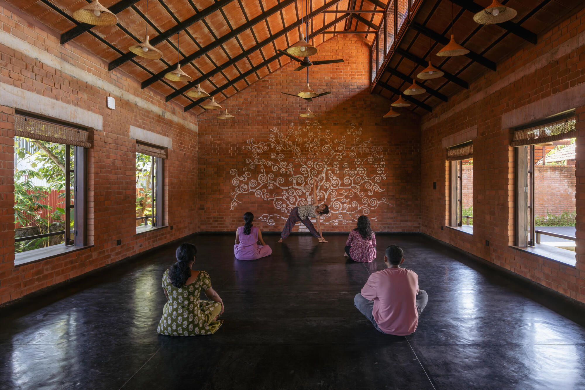 Vaulted brick room with patterned wall mural where seated figures gather on the polished floor
