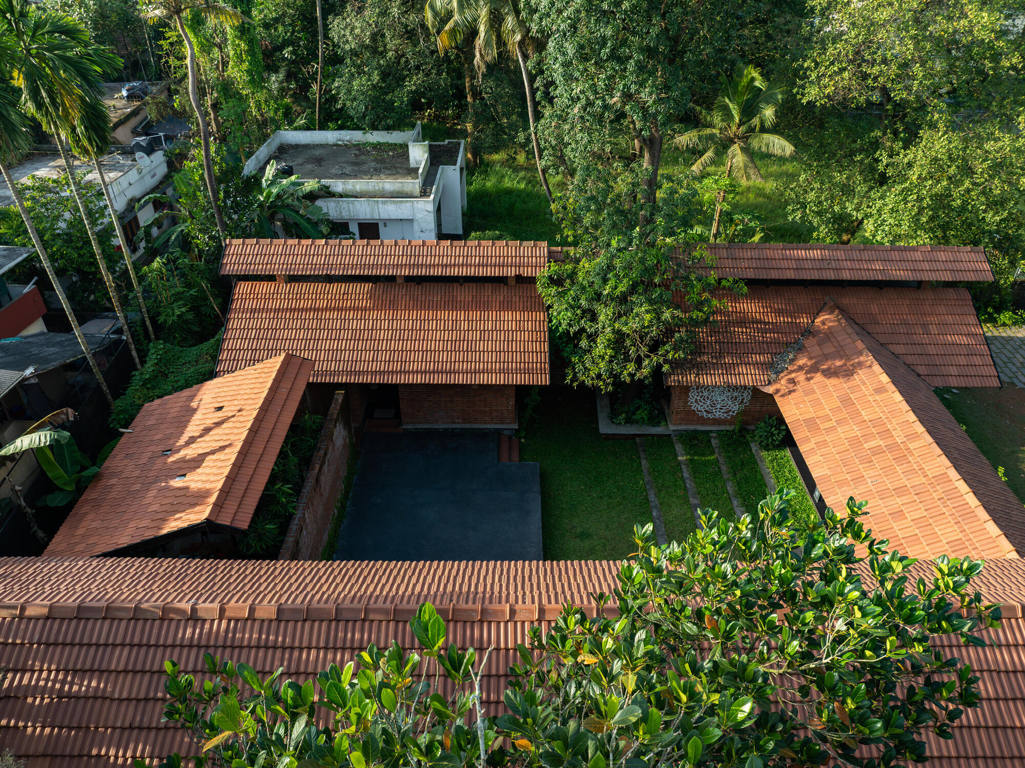 Drone view showing staggered clay tile rooflines around a courtyard with pool and palm trees