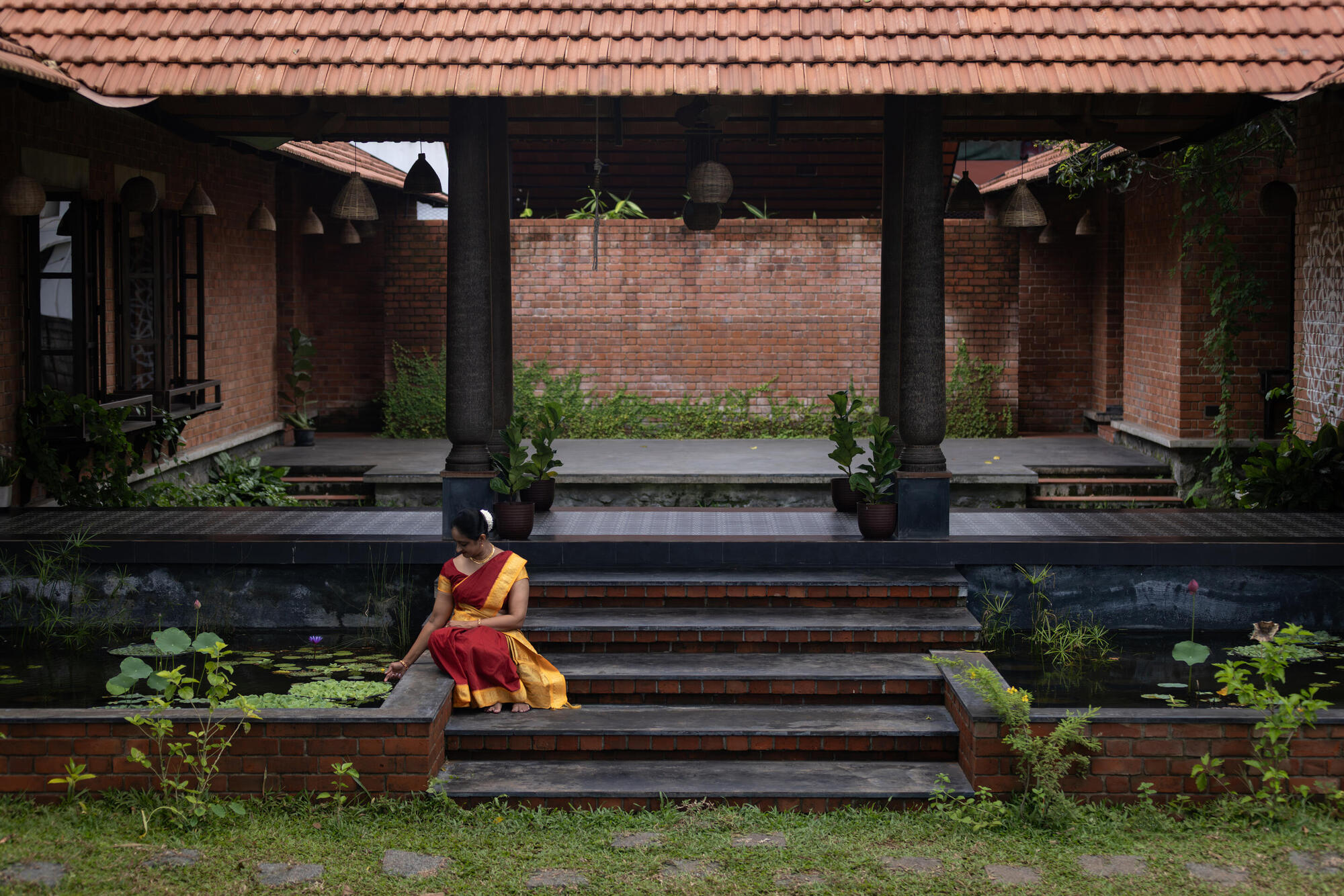 Person in red and yellow seated on dark brick steps beside a lily pond
