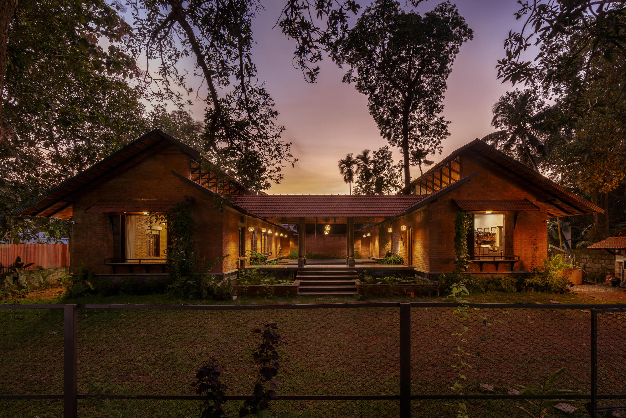 Symmetrical facade with two gabled brick wings flanking a central breezeway under overhanging trees at dusk