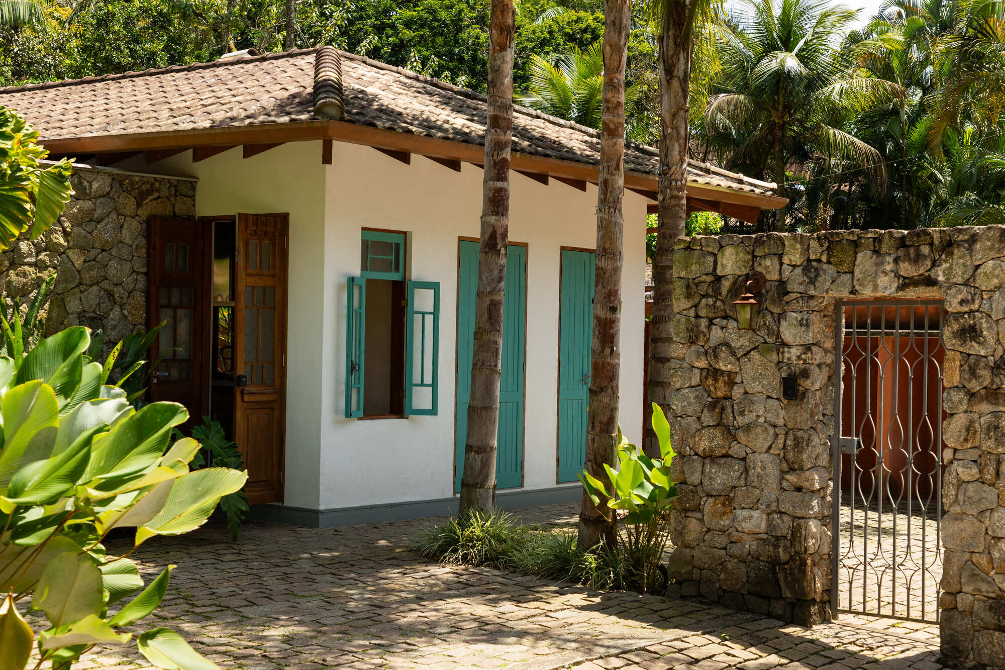 Courtyard entrance with wrought iron gate set within rough stone wall and tropical plantings
