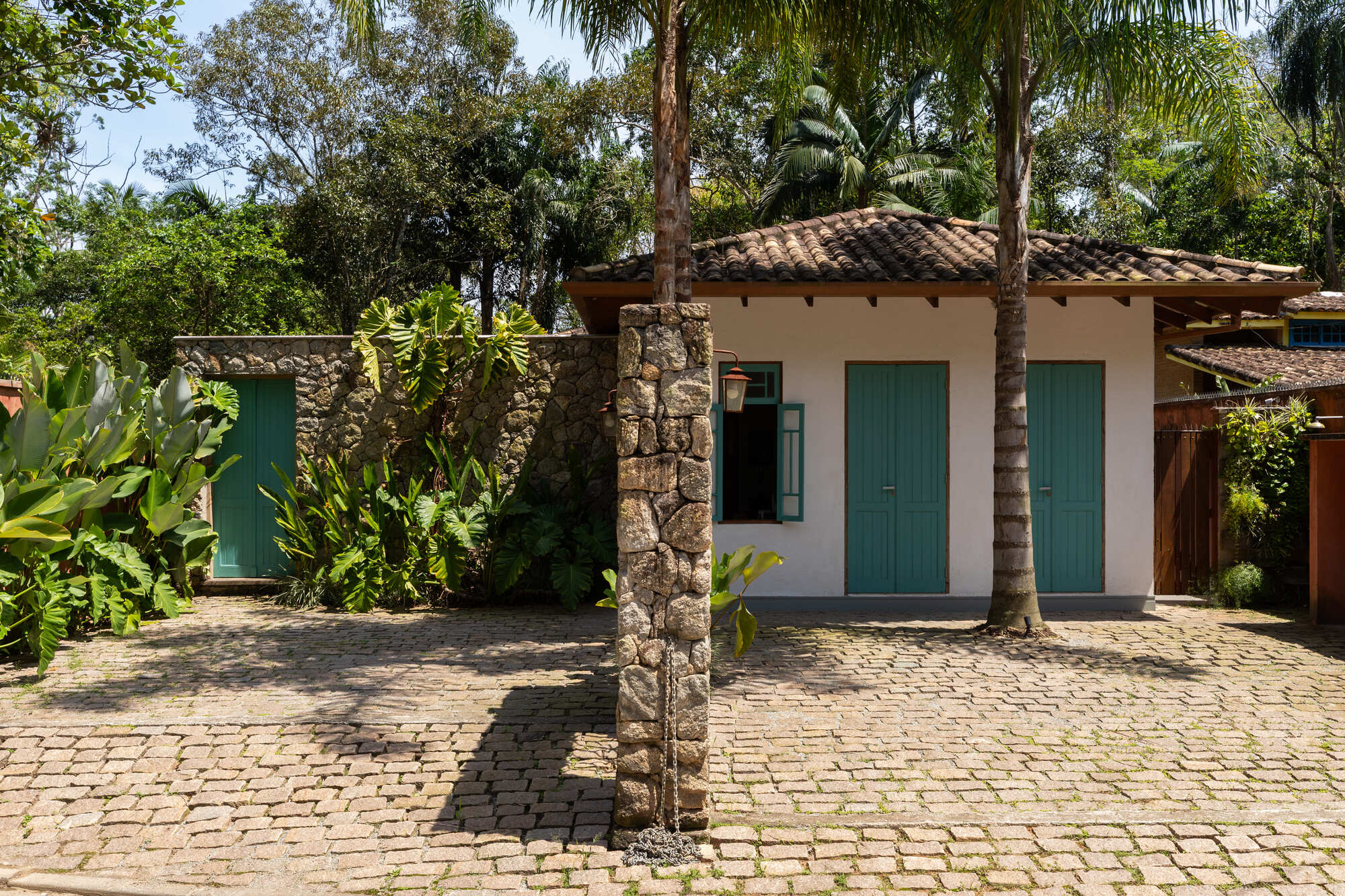 Street view of white volume with teal doors beyond stone piers and cobbled driveway