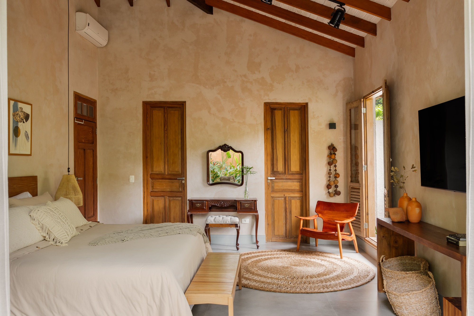 Bedroom with exposed timber rafters, pale plaster walls, and wooden doors framing an antique vanity