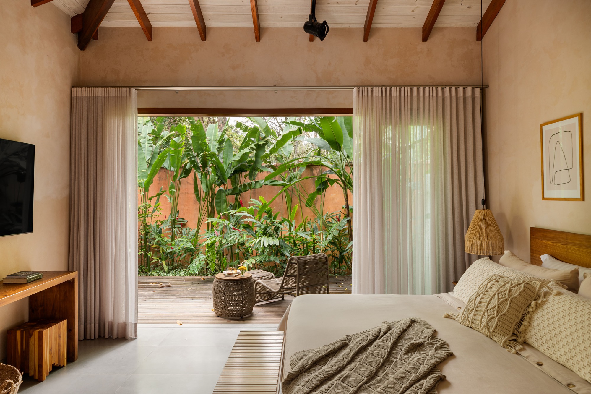 View through floor-to-ceiling glazed opening to planted courtyard with banana trees and terracotta wall