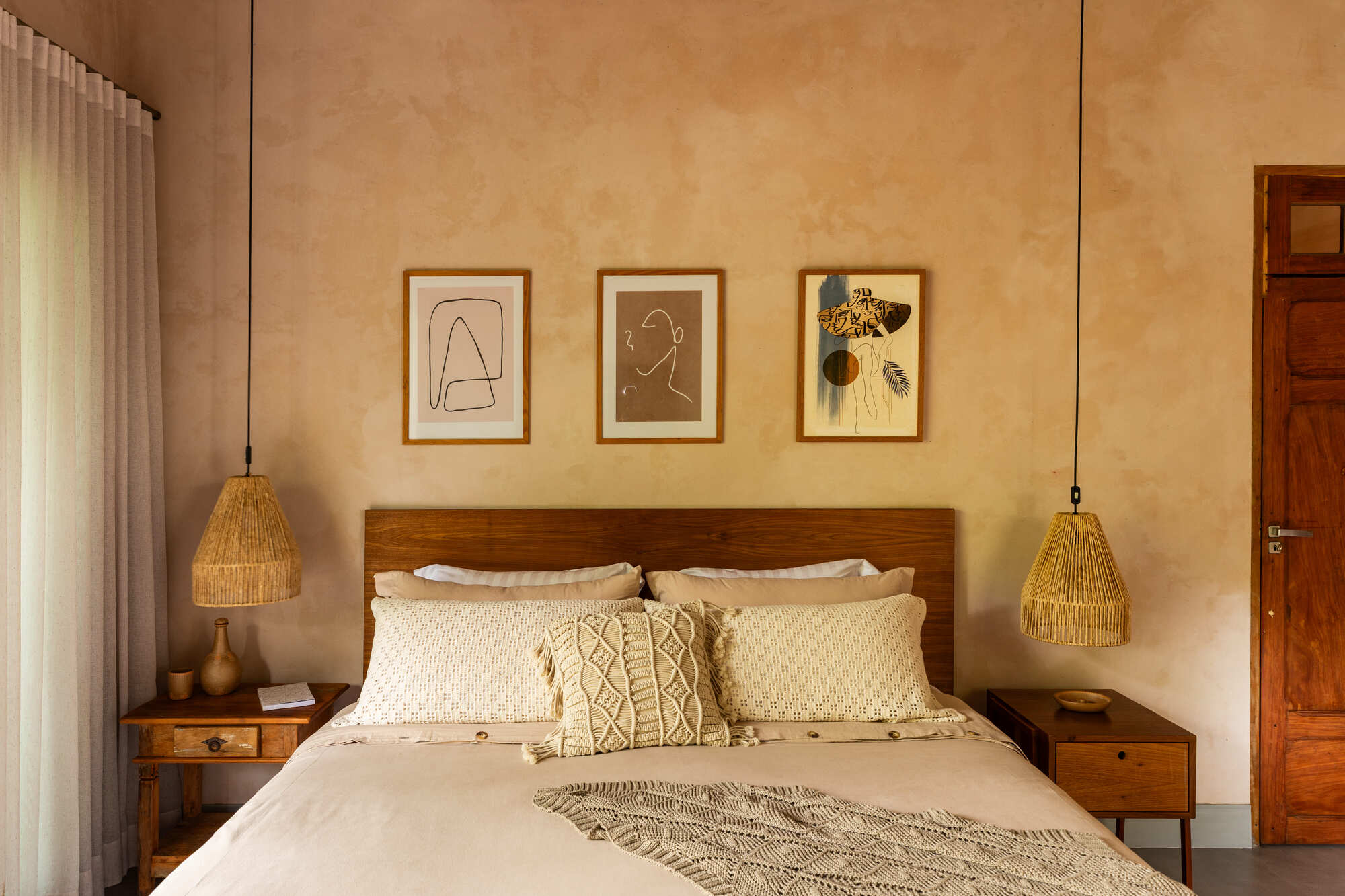 Timber headboard flanked by woven pendant lights and three framed artworks on plaster wall