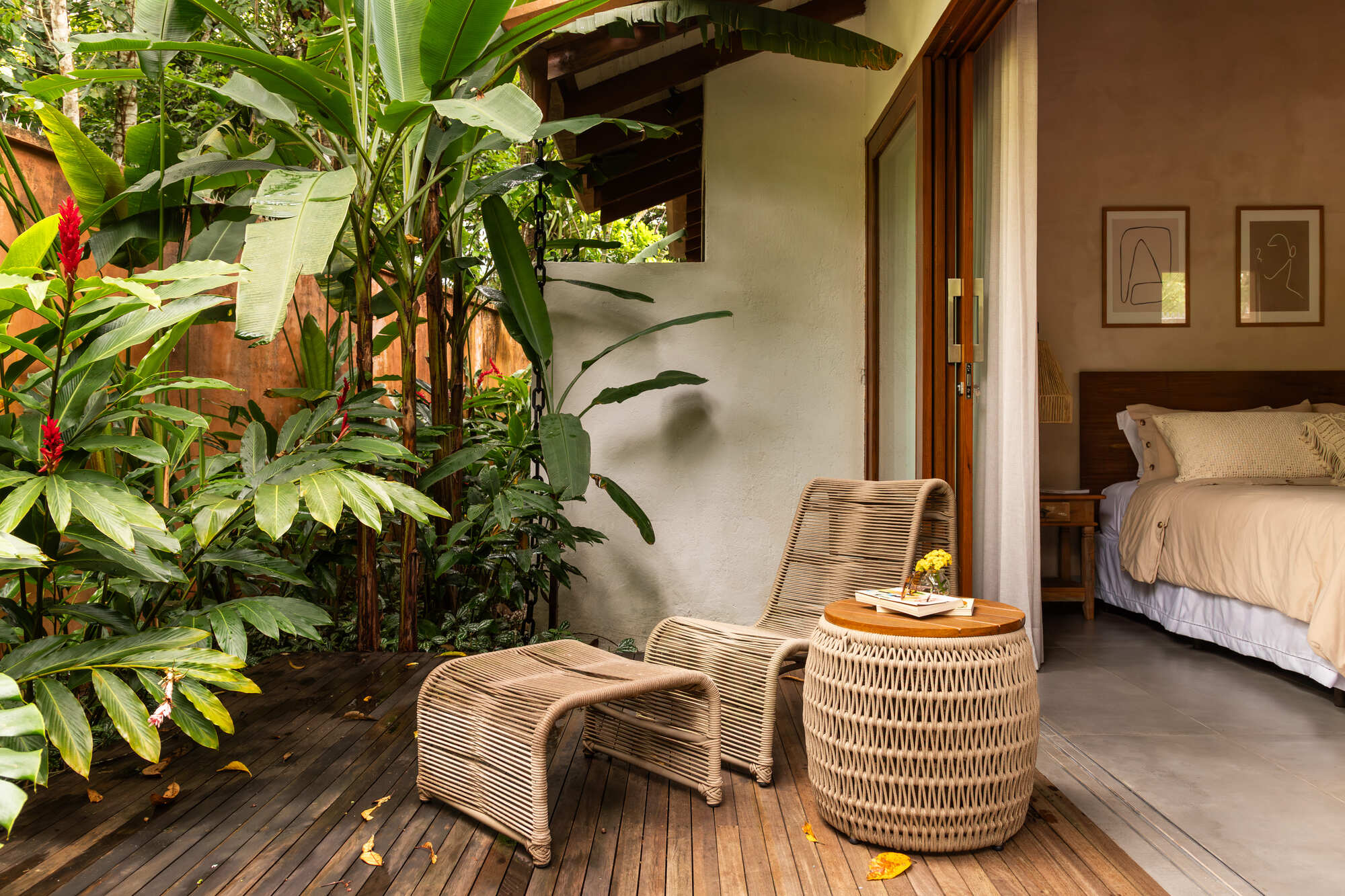 Timber deck terrace with woven lounge chair beside bedroom opening and heliconias in planted bed