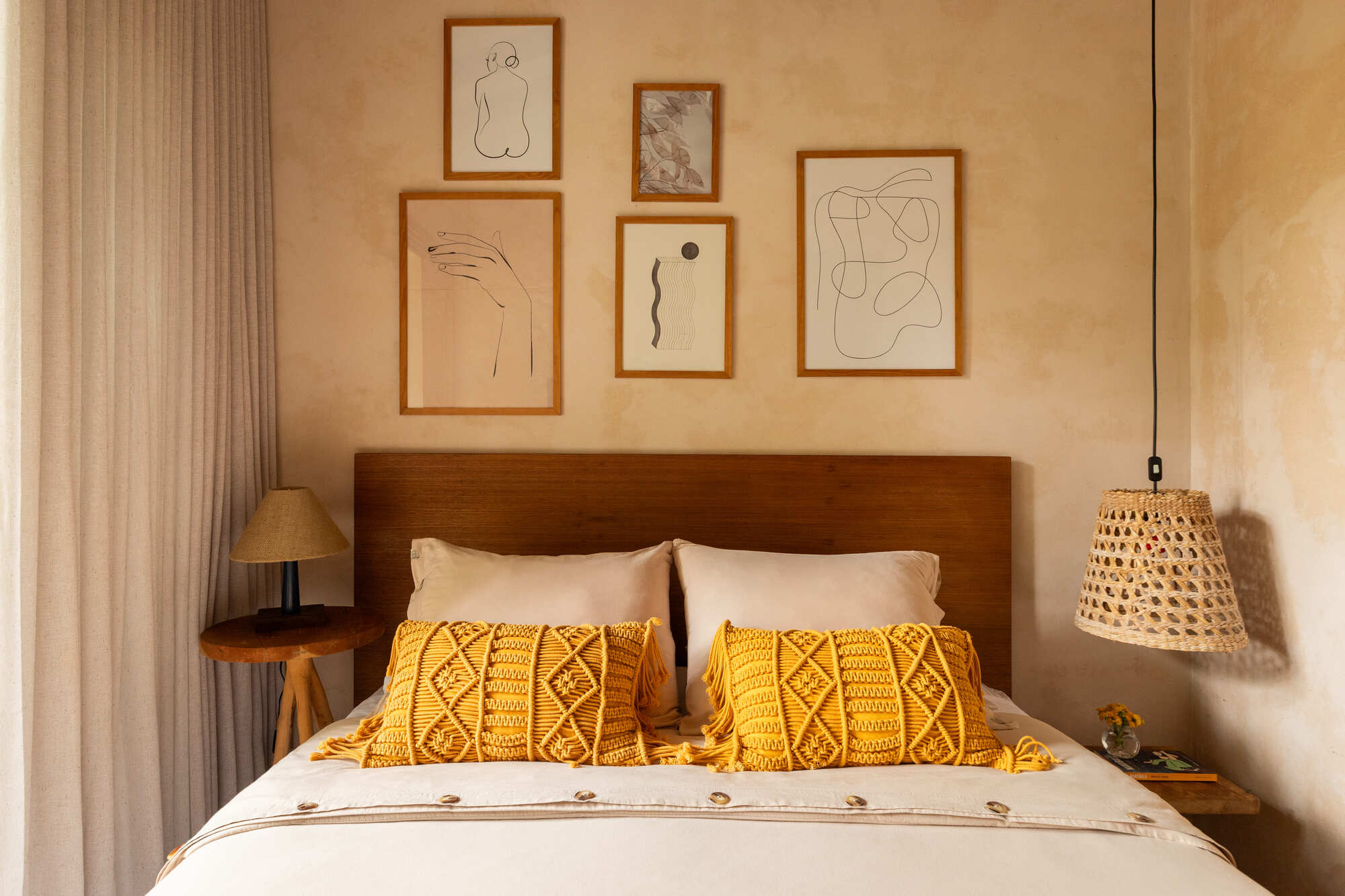 Bedroom wall with framed line drawings above a timber headboard and yellow patterned pillows
