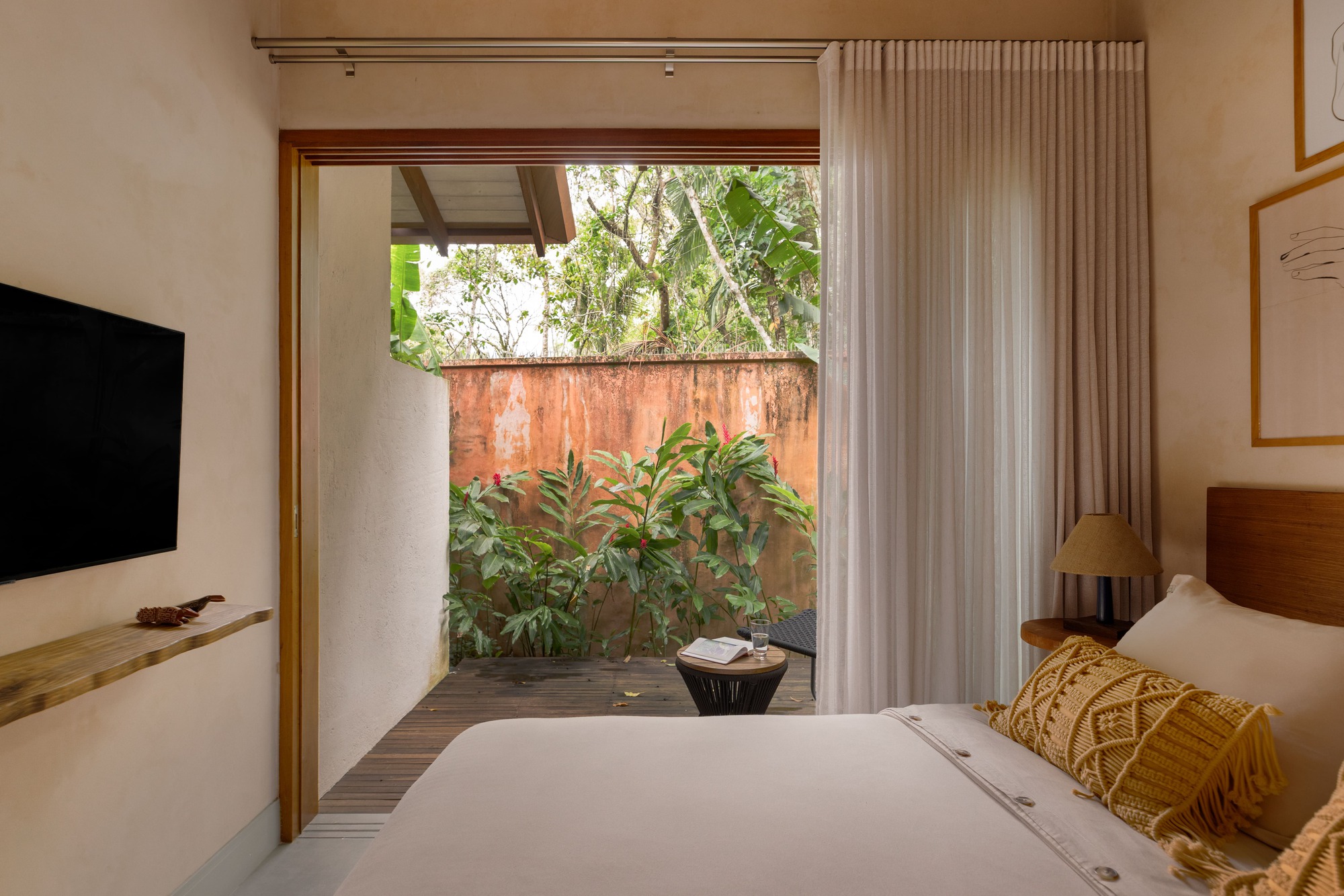 Glass door opening from bedroom to a planted courtyard with weathered copper wall and tropical vegetation