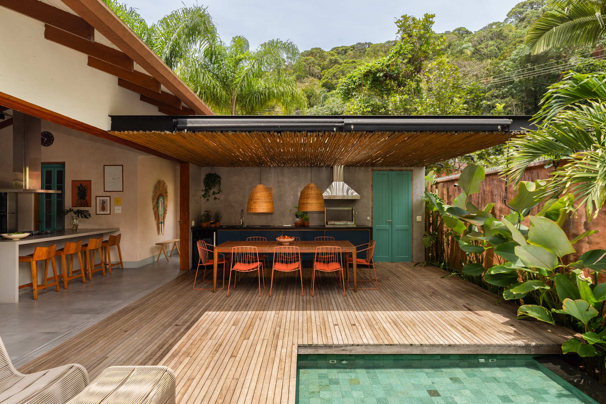 Covered outdoor dining terrace with bamboo pergola, woven pendant lamps and swimming pool edge surrounded by palms