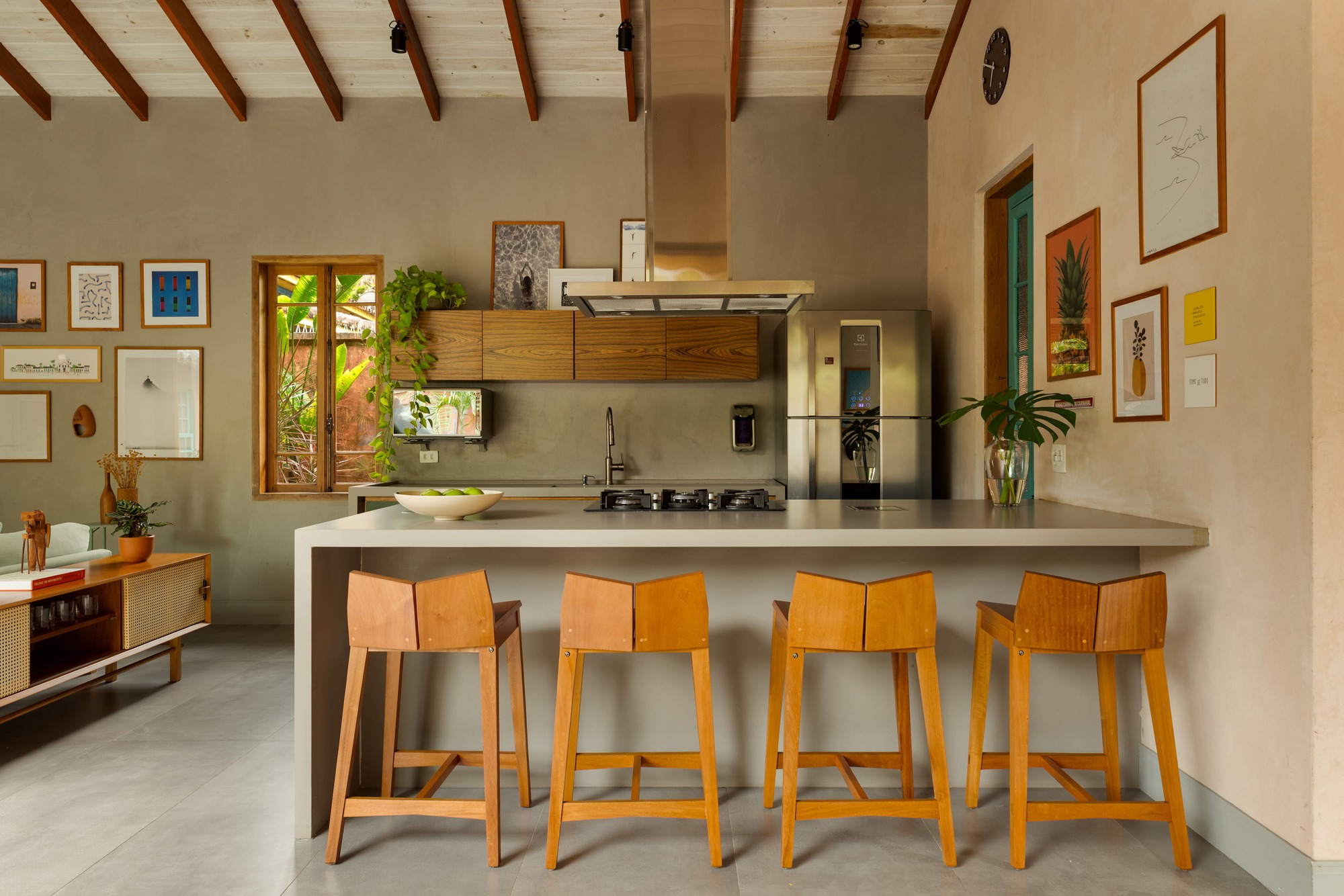 Kitchen island with four wooden bar stools beneath exposed timber rafters and polished concrete floor
