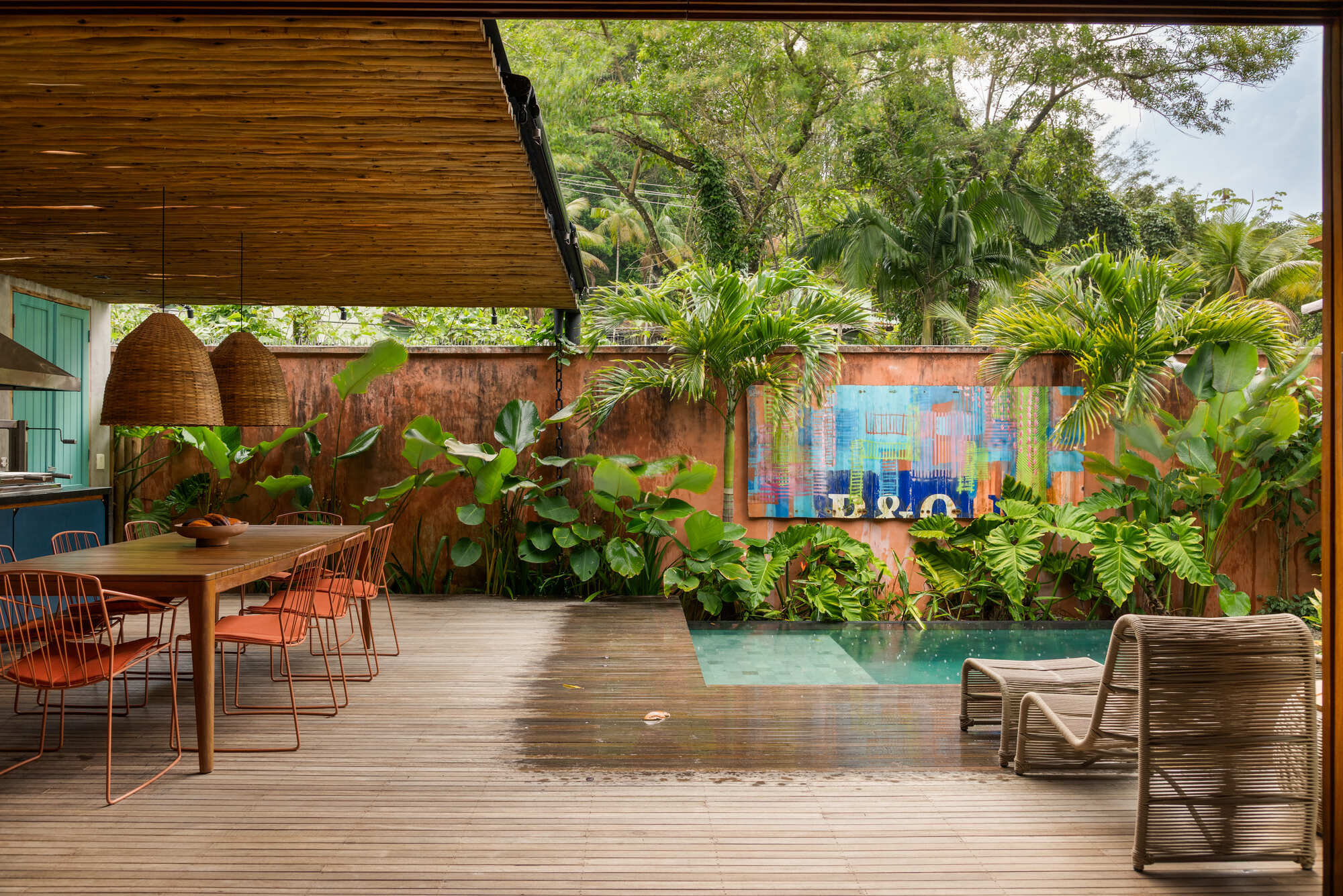 Covered timber deck with pool alongside planted beds and colorful tile mural on boundary wall