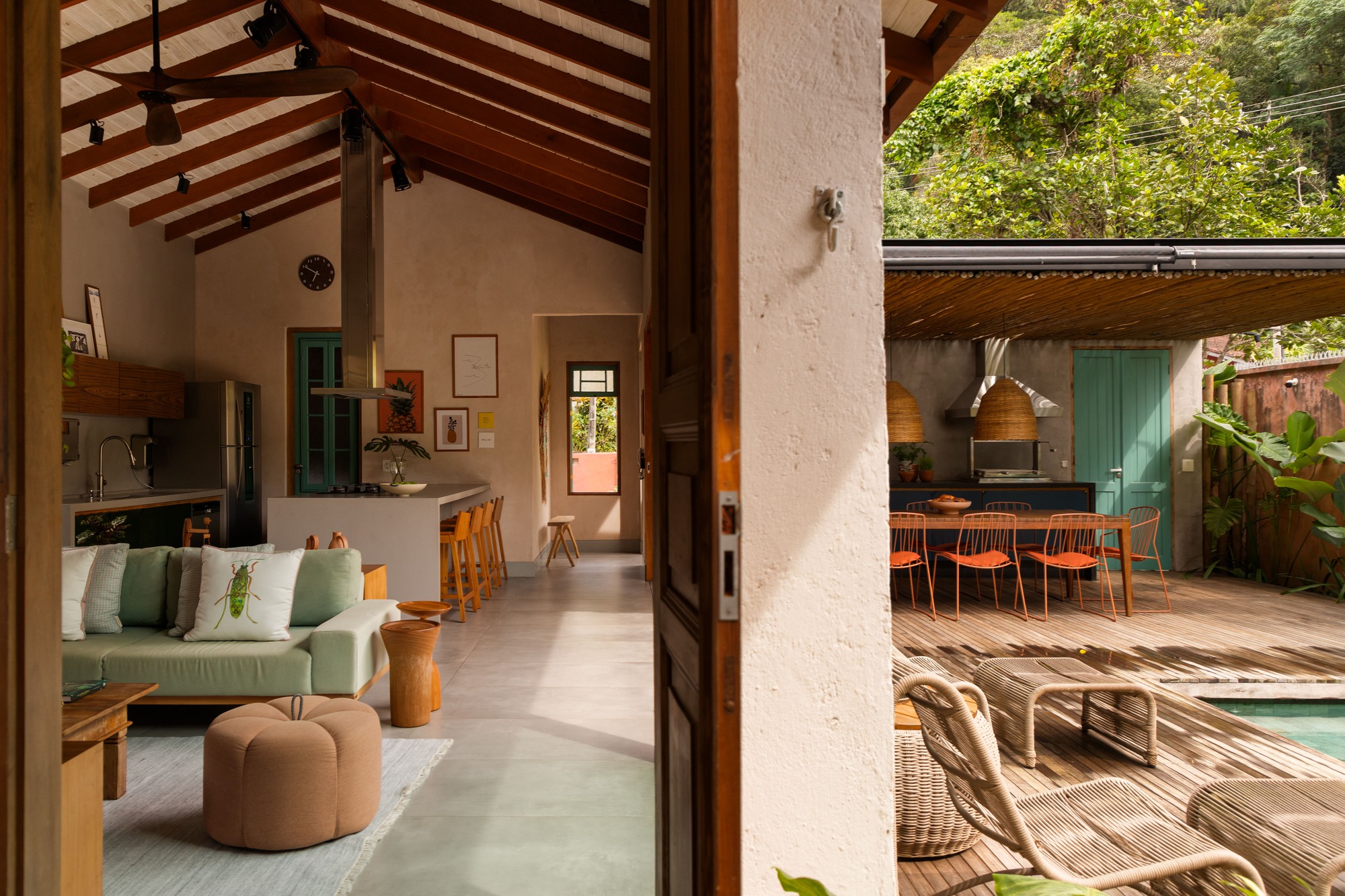 View through open timber door to living area and outdoor deck with pool under dappled sunlight