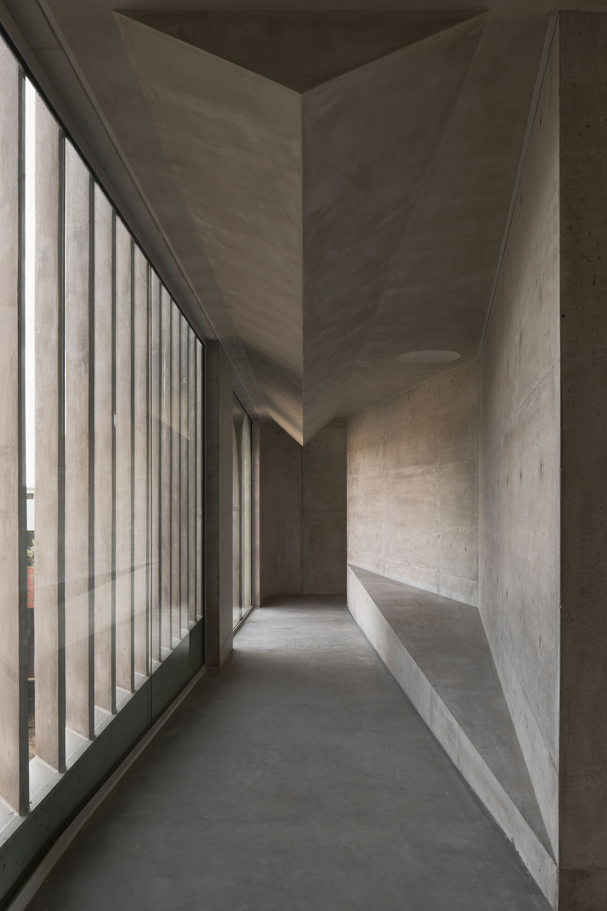 Concrete corridor with vertical louvered glazing filtering natural light along one side