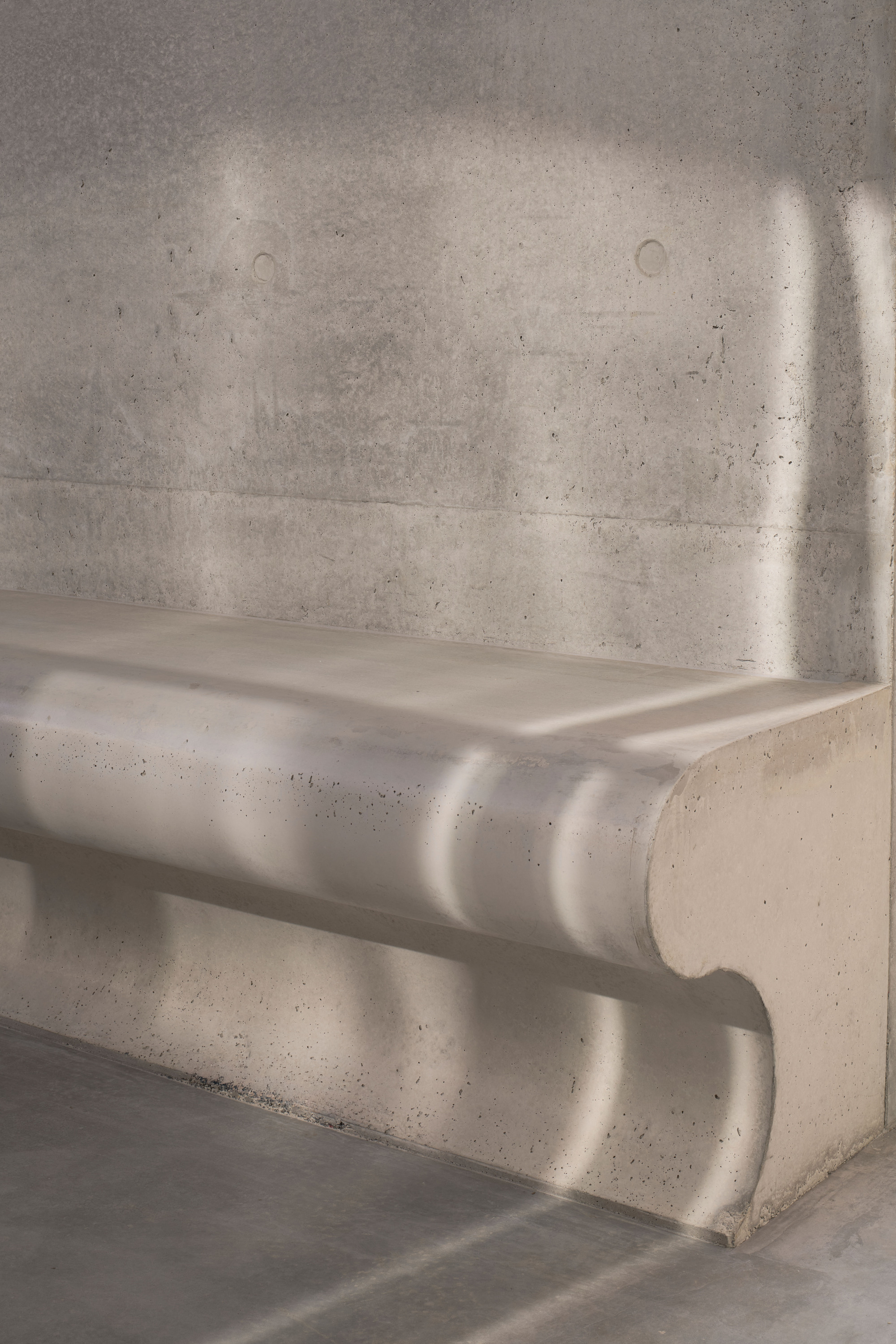 Close-up of board-formed concrete stair treads with dappled sunlight across the surface