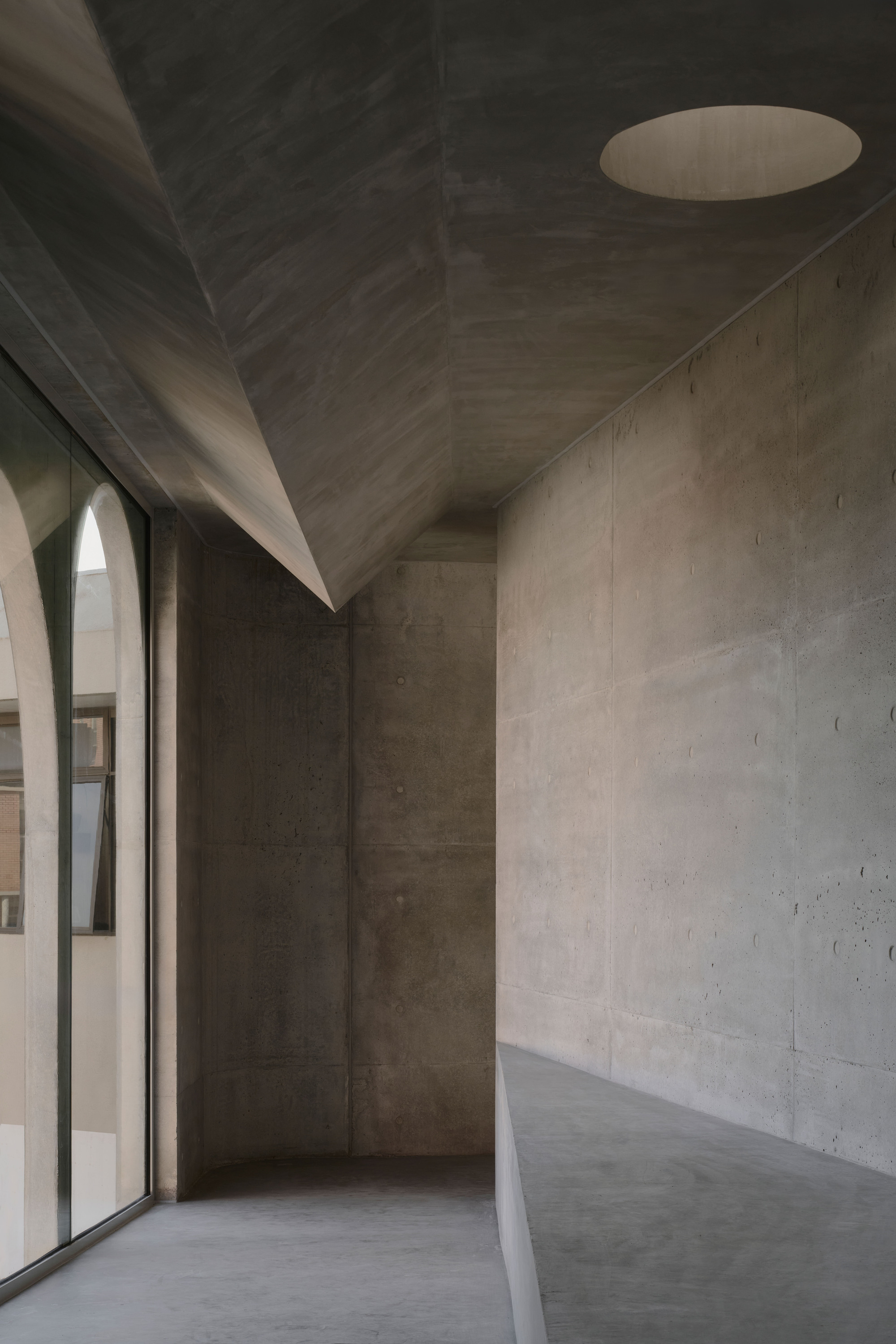 Board-formed concrete interior space with folded ceiling planes and a circular skylight