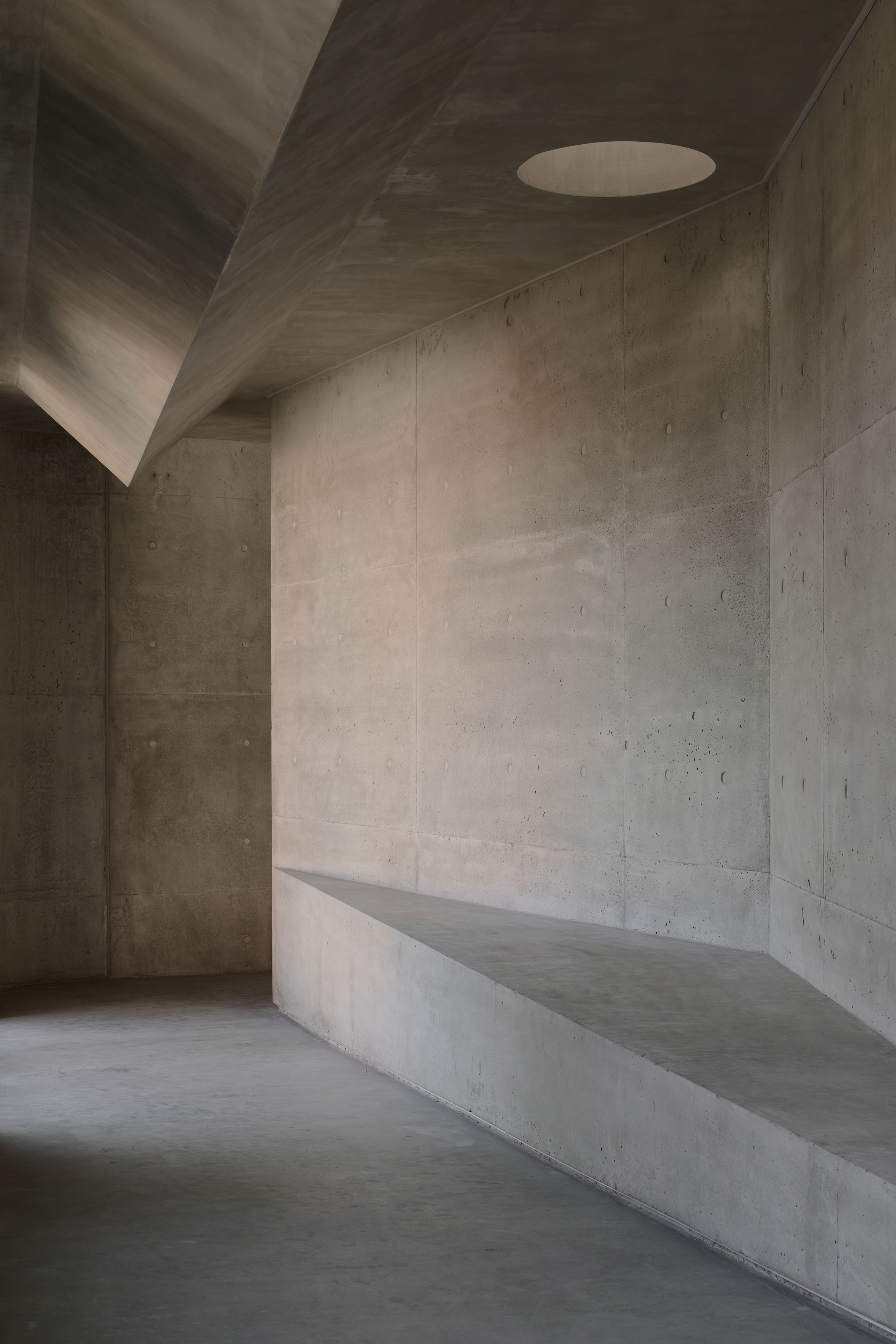 Concrete interior corner with built-in bench and angular ceiling planes in soft daylight