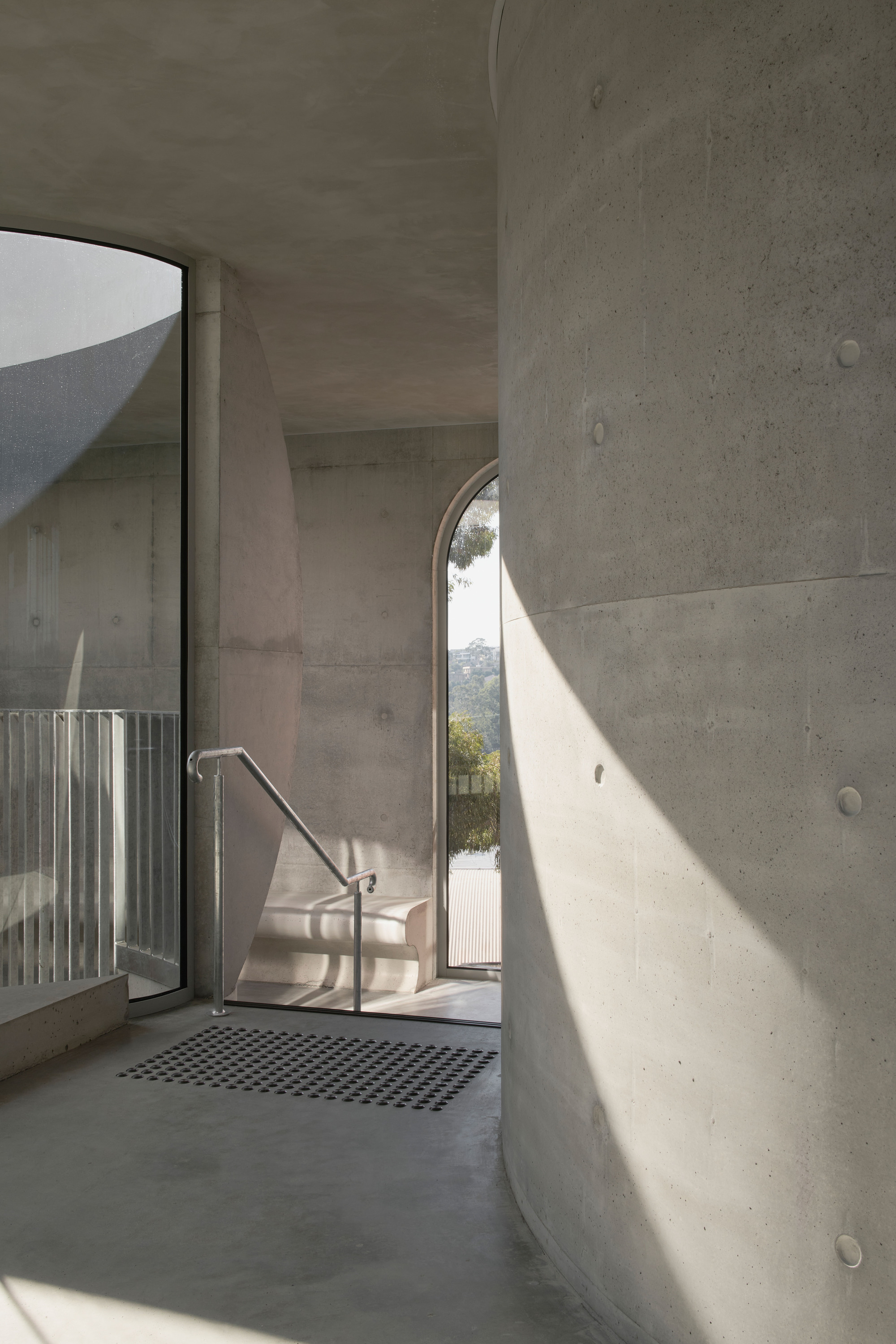 Concrete interior with arched doorway casting sunlight onto the walls and metal grate floor