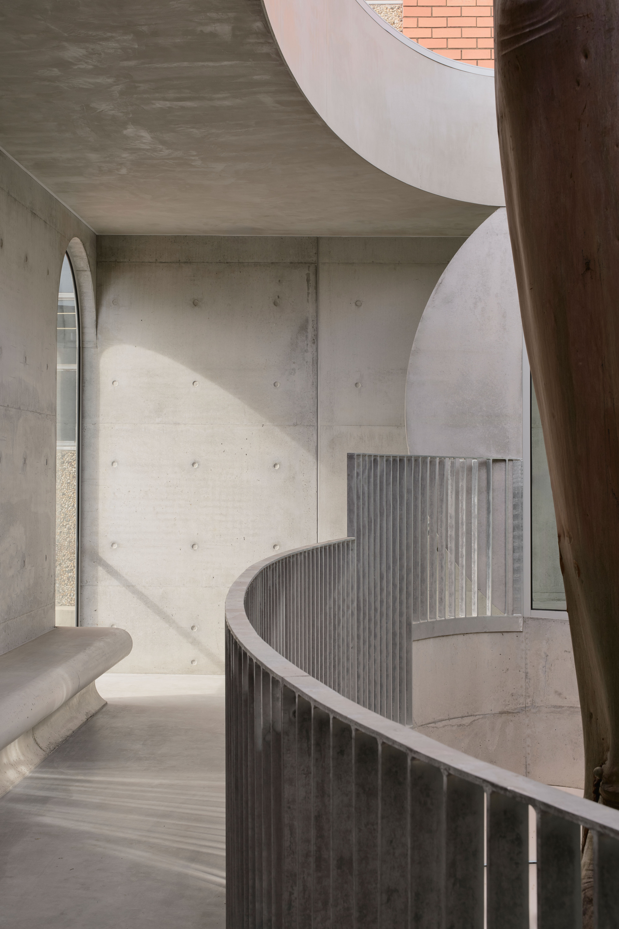Helical concrete staircase with vertical balustrade wrapping around a timber column in daylight