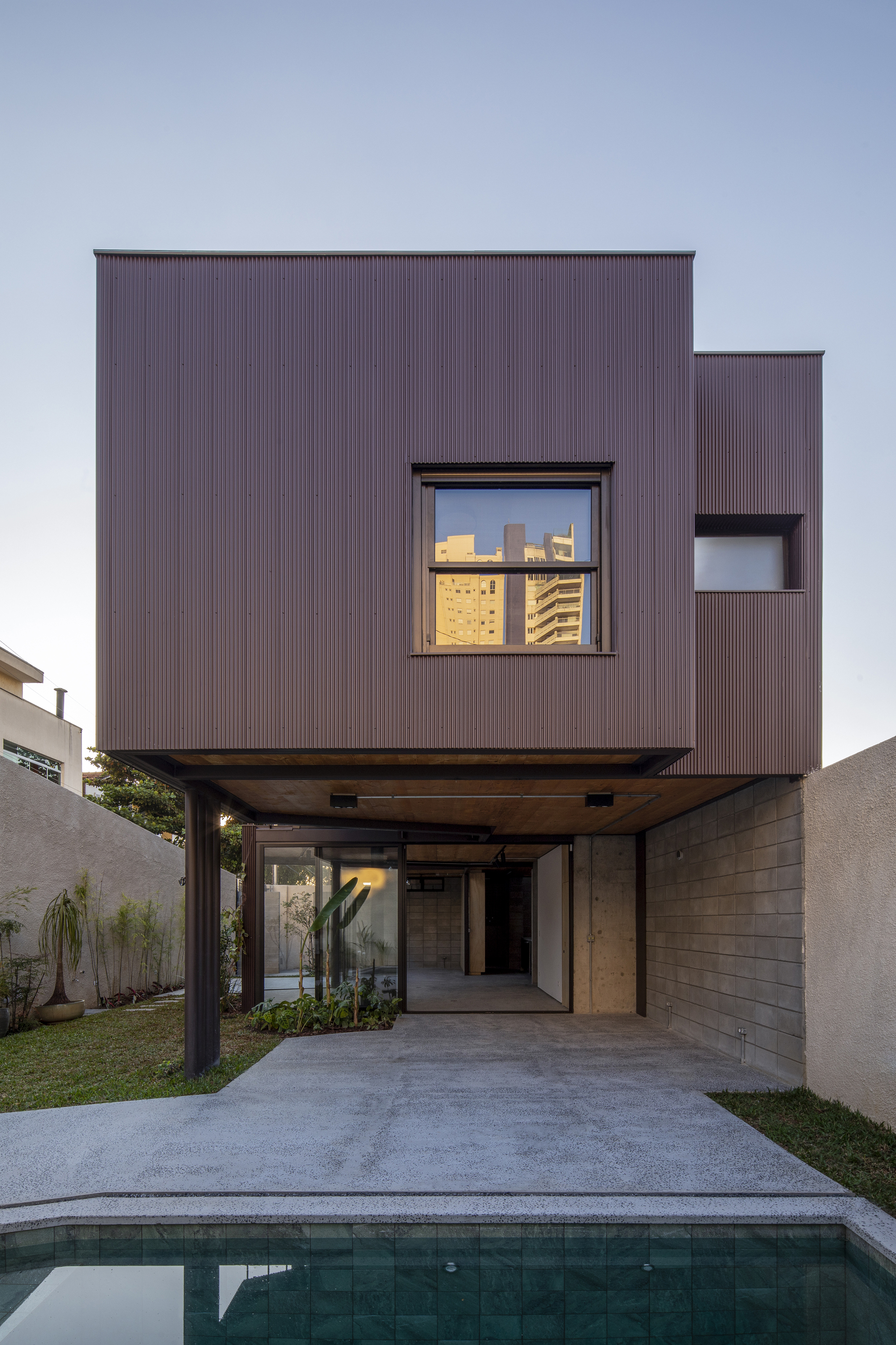 Pool deck view showing corrugated metal facade elevated on steel columns at twilight