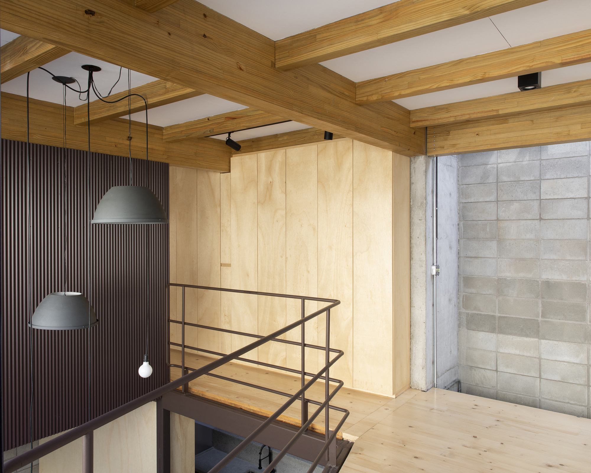 Upper level passage with plywood storage volume and steel railing overlooking lower space