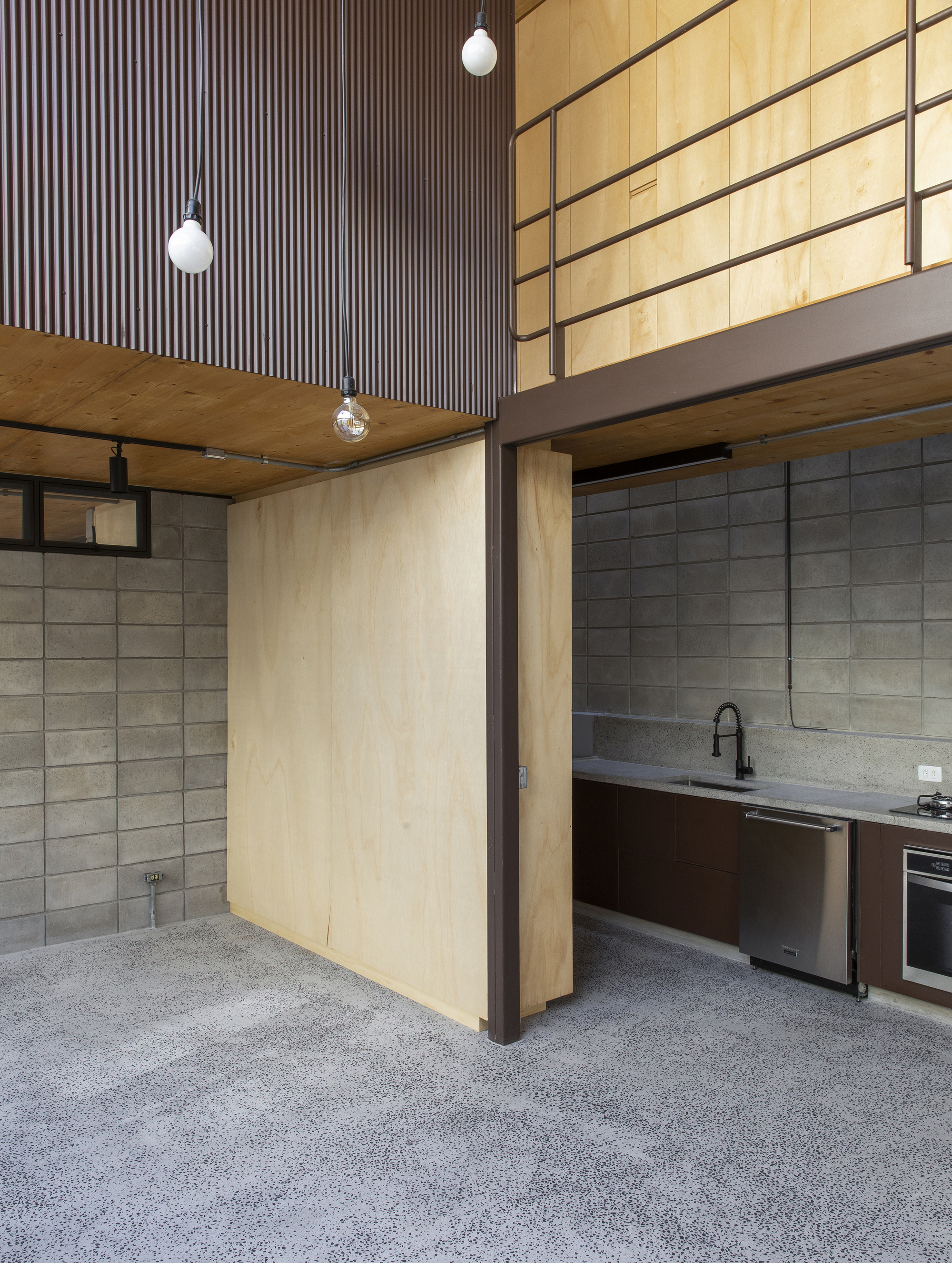 Kitchen counter with concrete block walls, plywood cabinetry and mezzanine guardrail under pendant lighting