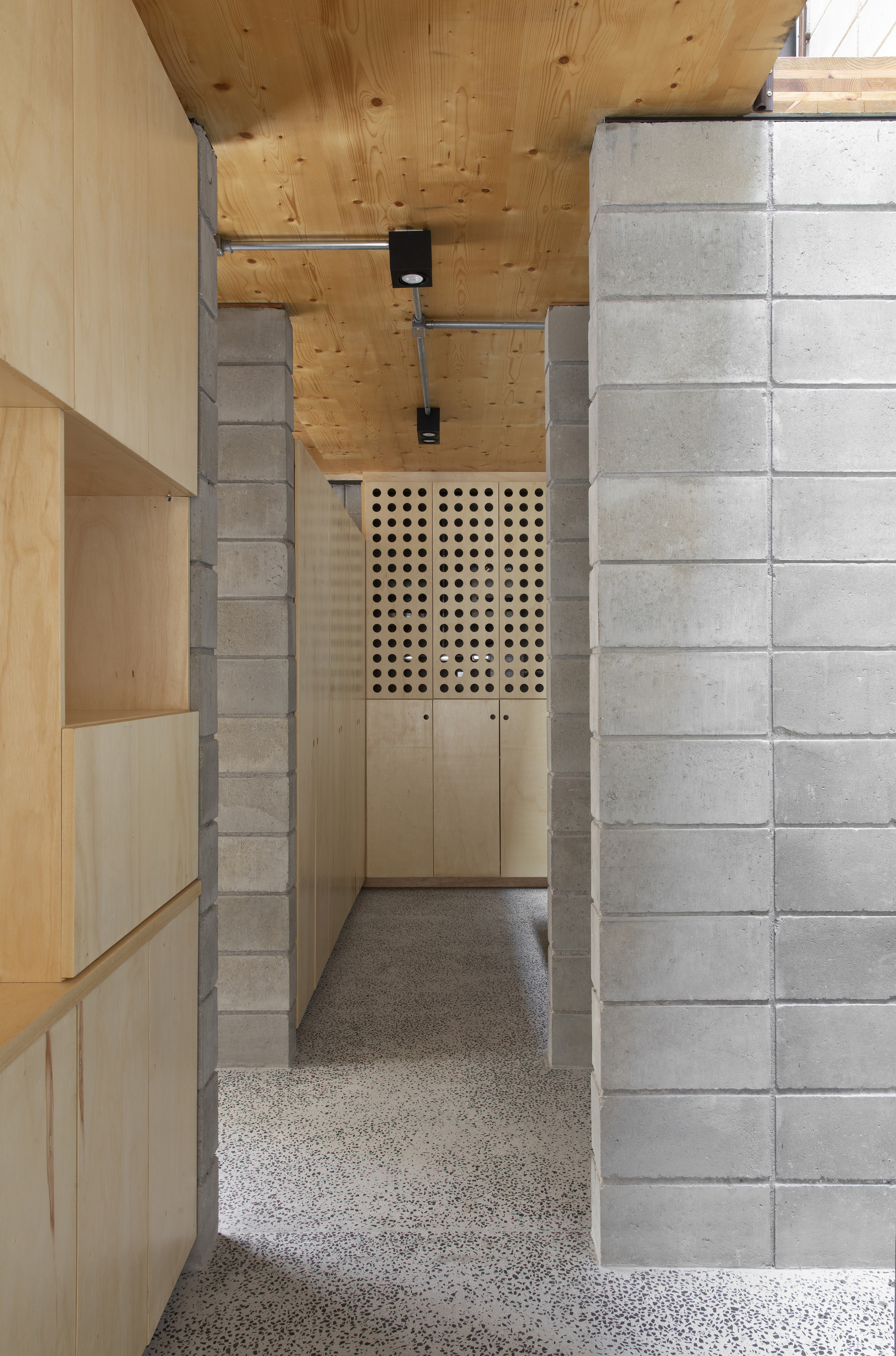 Corridor view through concrete block walls toward plywood storage with perforated door panel