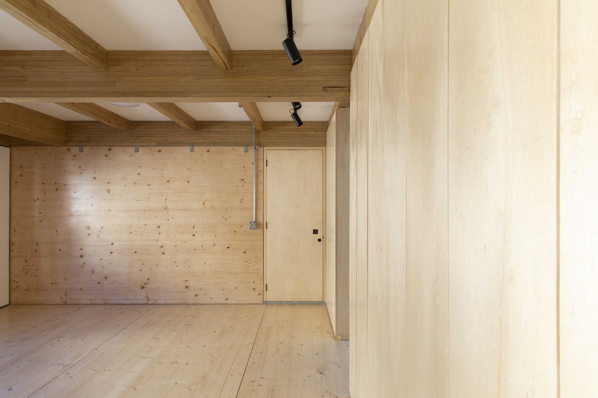 Interior room with exposed timber ceiling beams, light wood plank walls and floor-to-ceiling wood partition wall