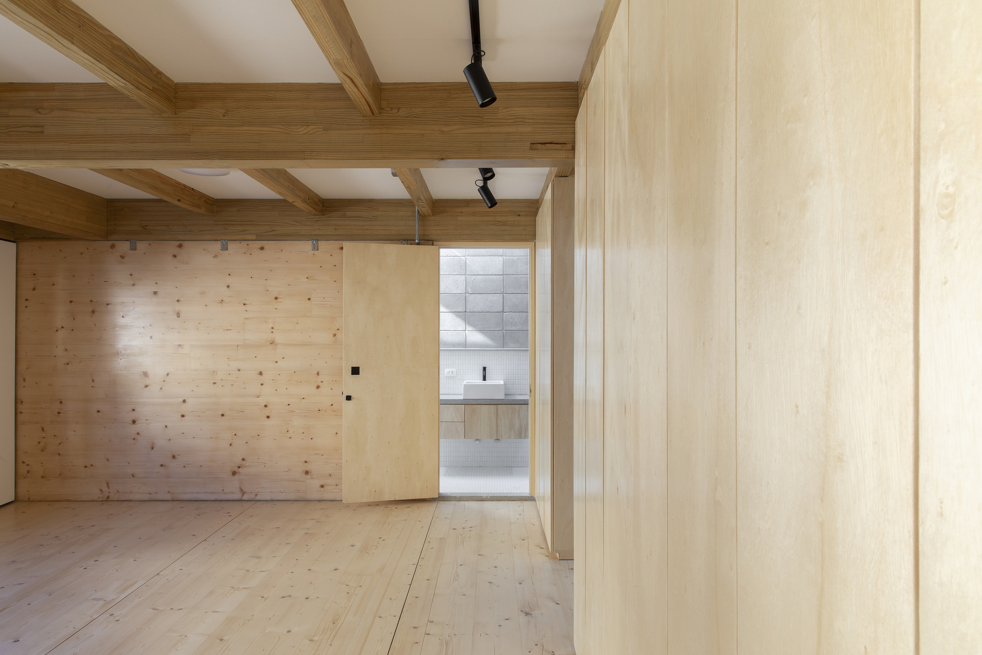 View through open doorway revealing white-tiled bathroom beyond timber-lined interior with exposed beam ceiling