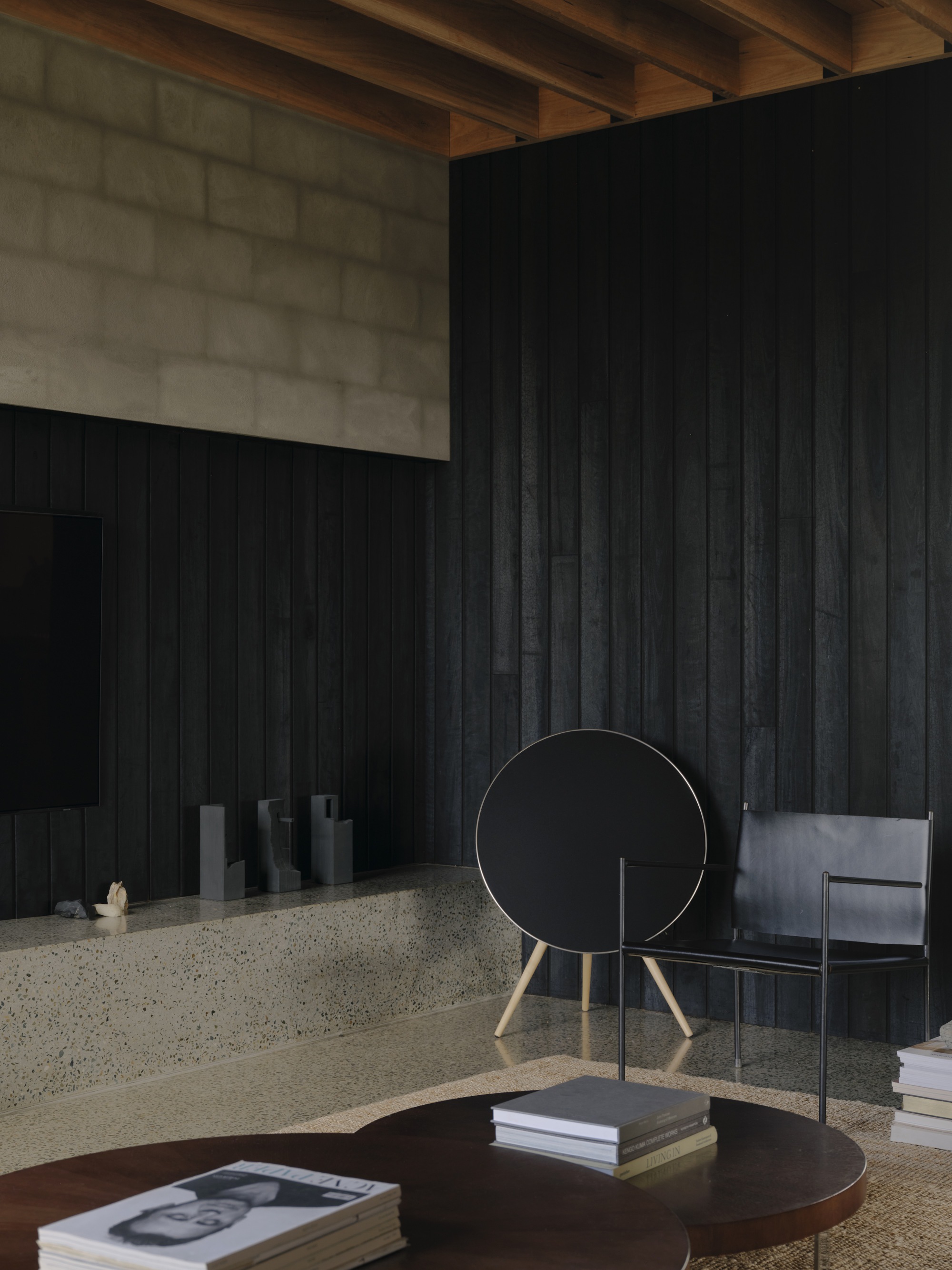 Interior corner showing charred timber wall panels meeting concrete wall beneath exposed timber ceiling joists