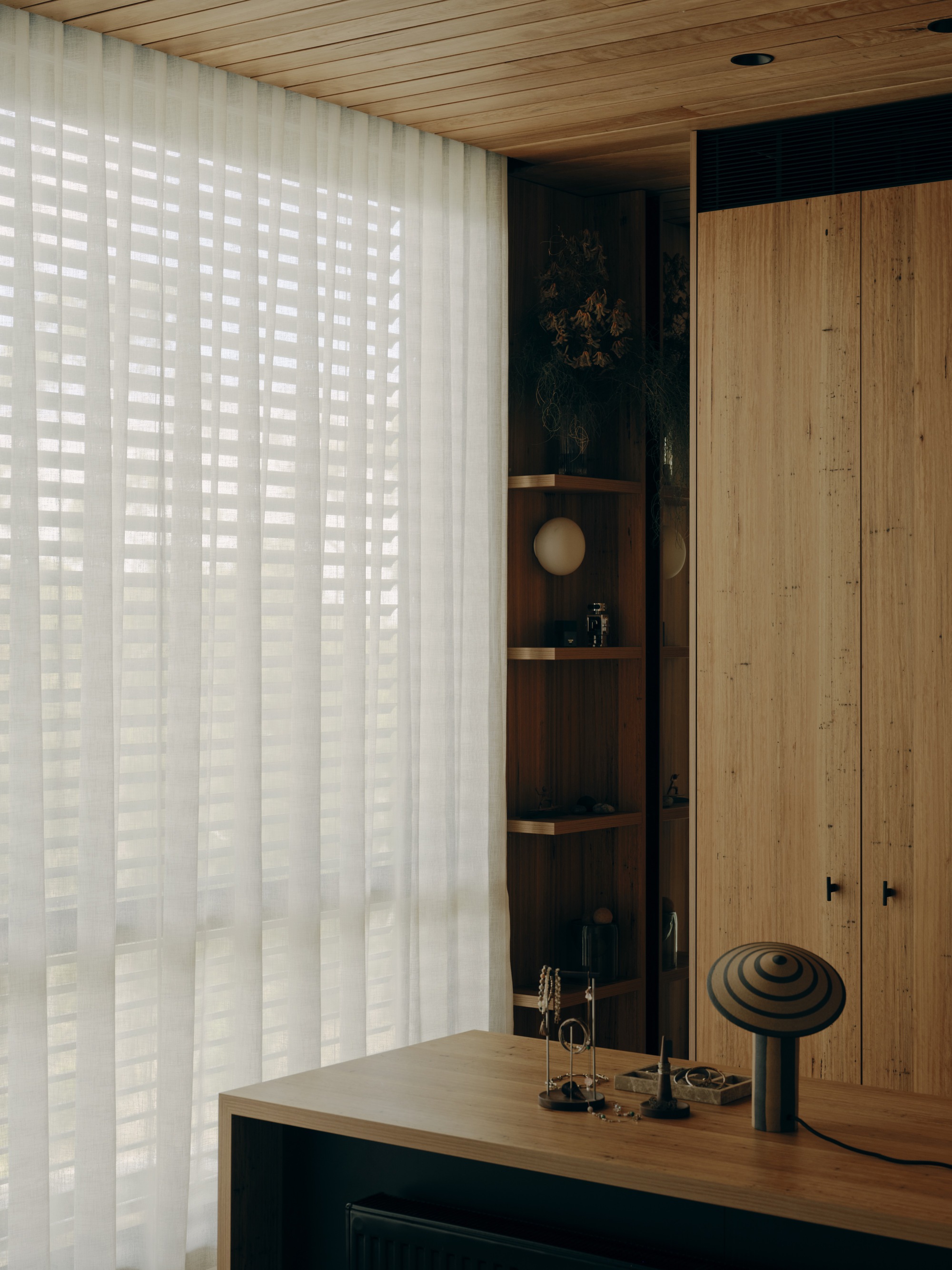 Timber desk with sculptural objects against backlit vertical blinds and a recessed display niche