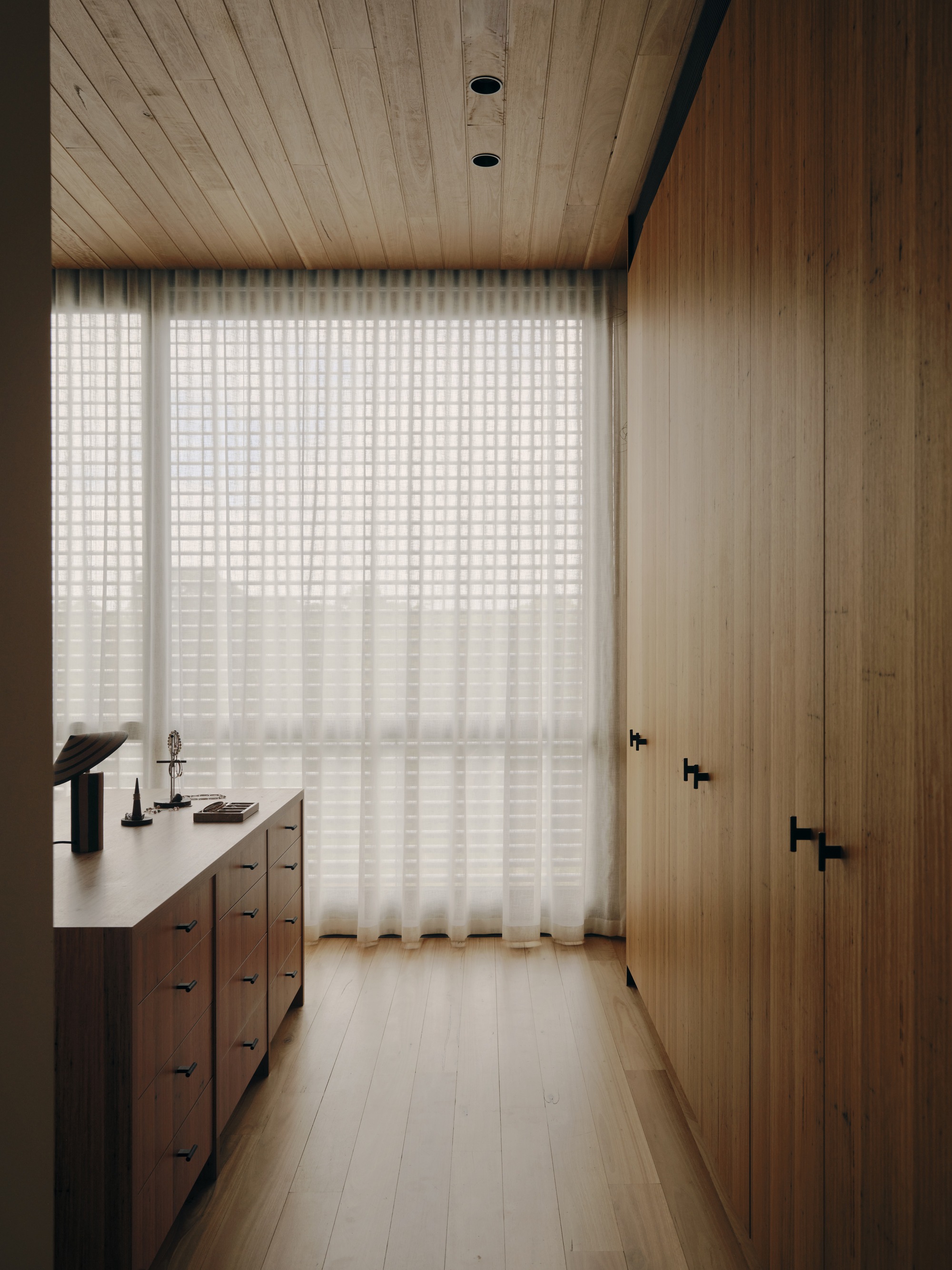 Narrow hallway with timber-lined ceiling, translucent grid curtain filtering daylight, and a built-in credenza