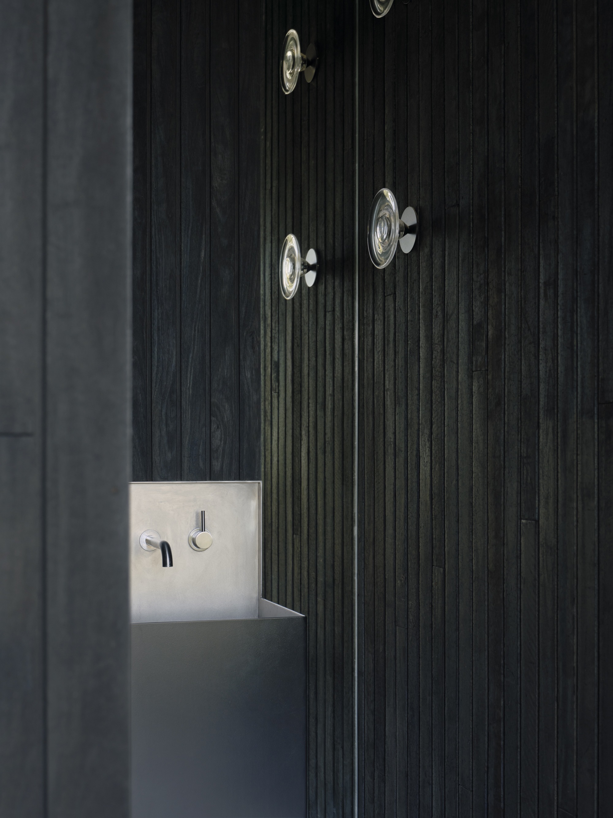 Detail of charred vertical timber cladding with embedded brass light switches and knotted wood grain