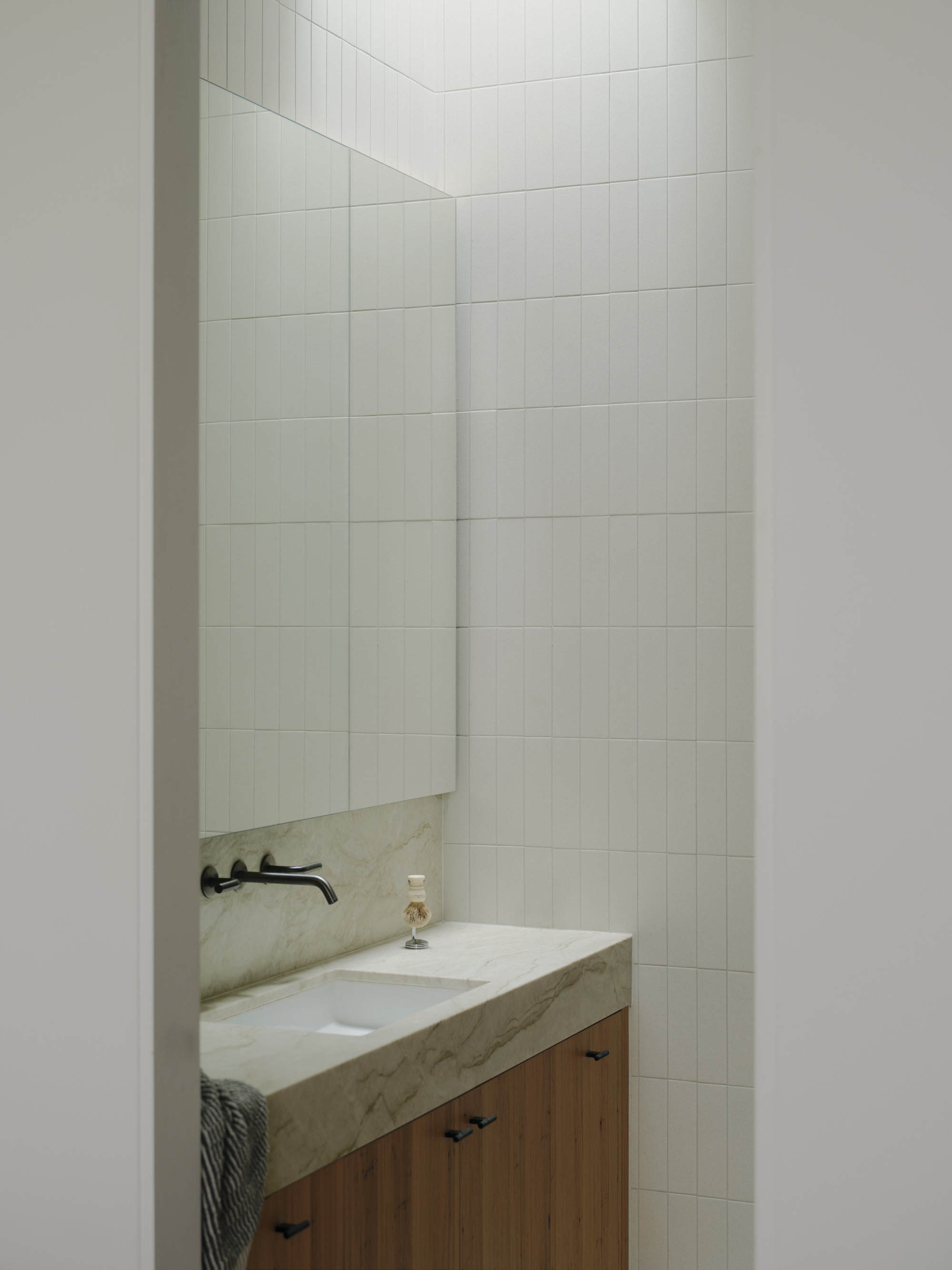 Bathroom vanity with stone countertop and timber cabinetry framed by large-format white tile walls