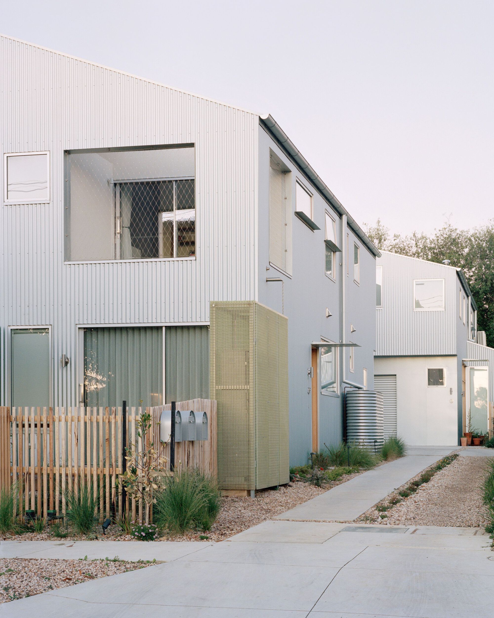 Entry pathway showing corrugated cladding with olive panels and timber screens beside planted gravel beds