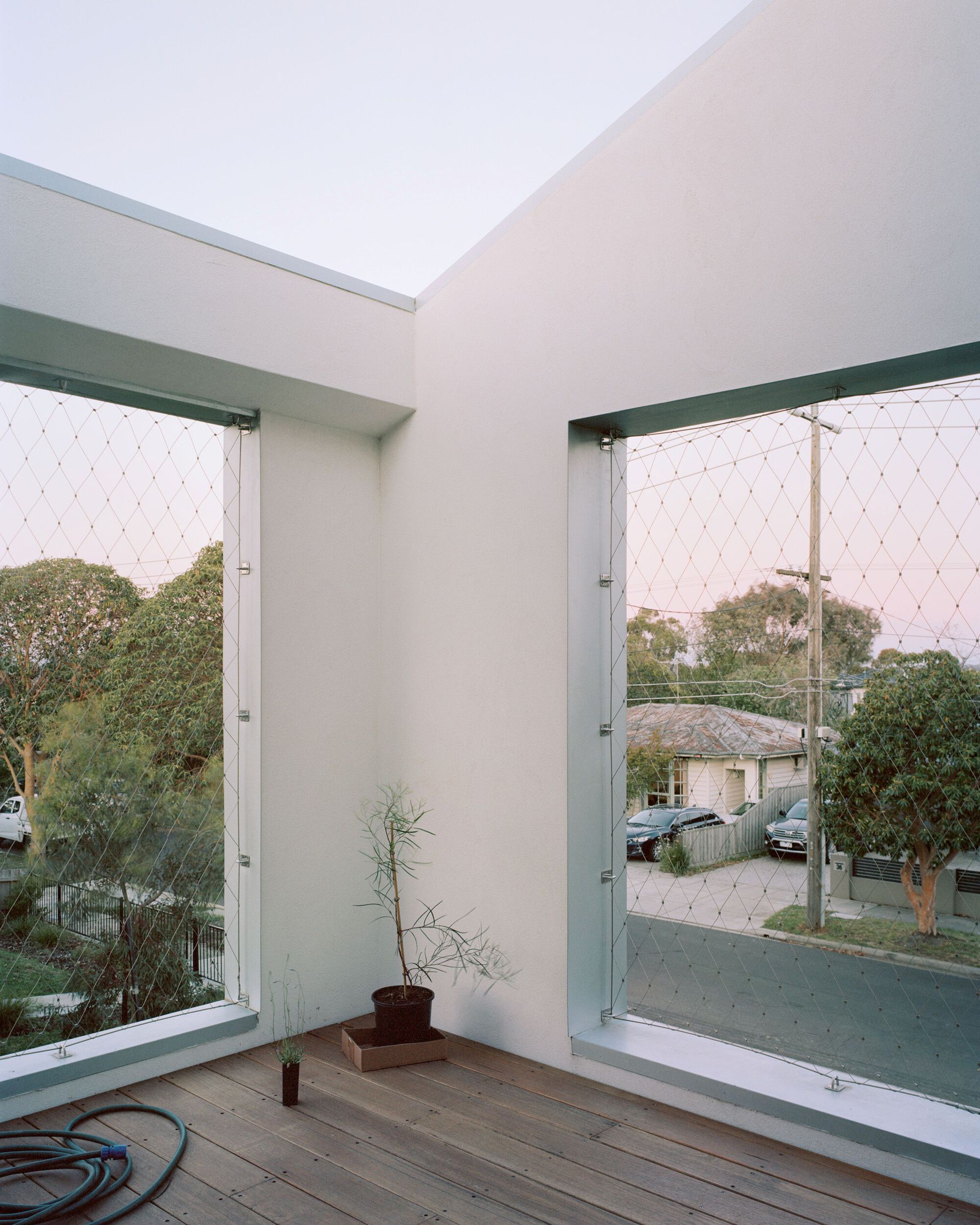 Corner balcony with timber decking and mesh safety screens framing views to the street