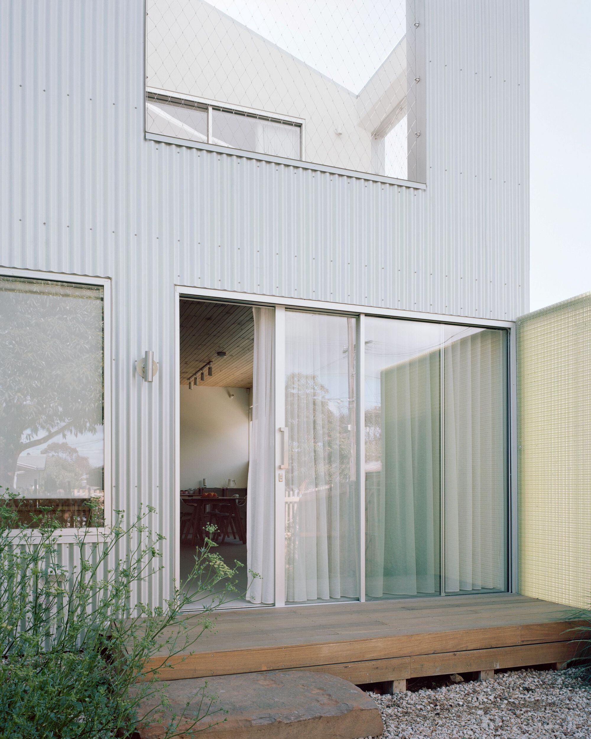 Courtyard with sliding glass doors opening from corrugated walls onto a timber deck and gravel