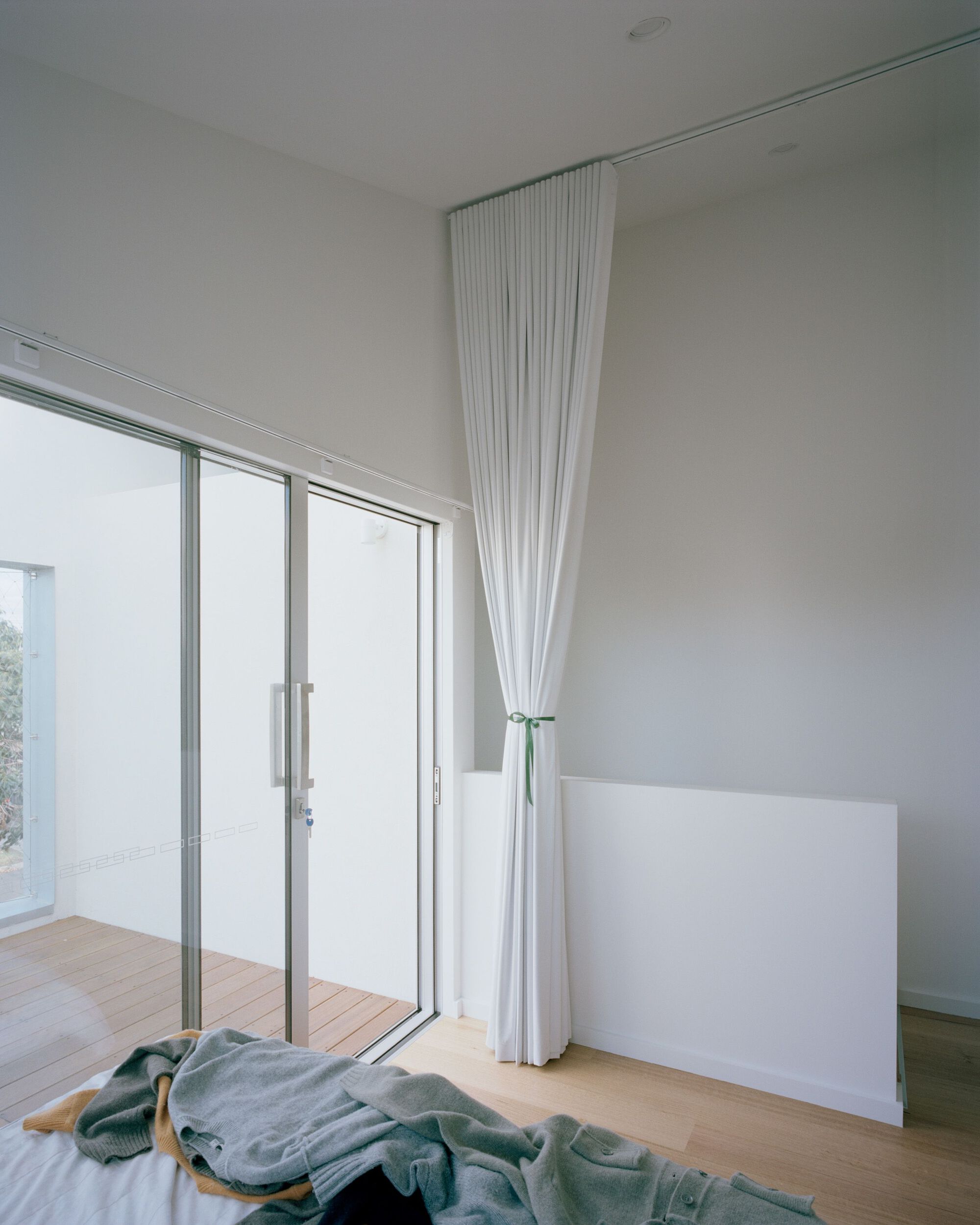 Bedroom corner with full-height curtain beside glazed doors opening to timber deck