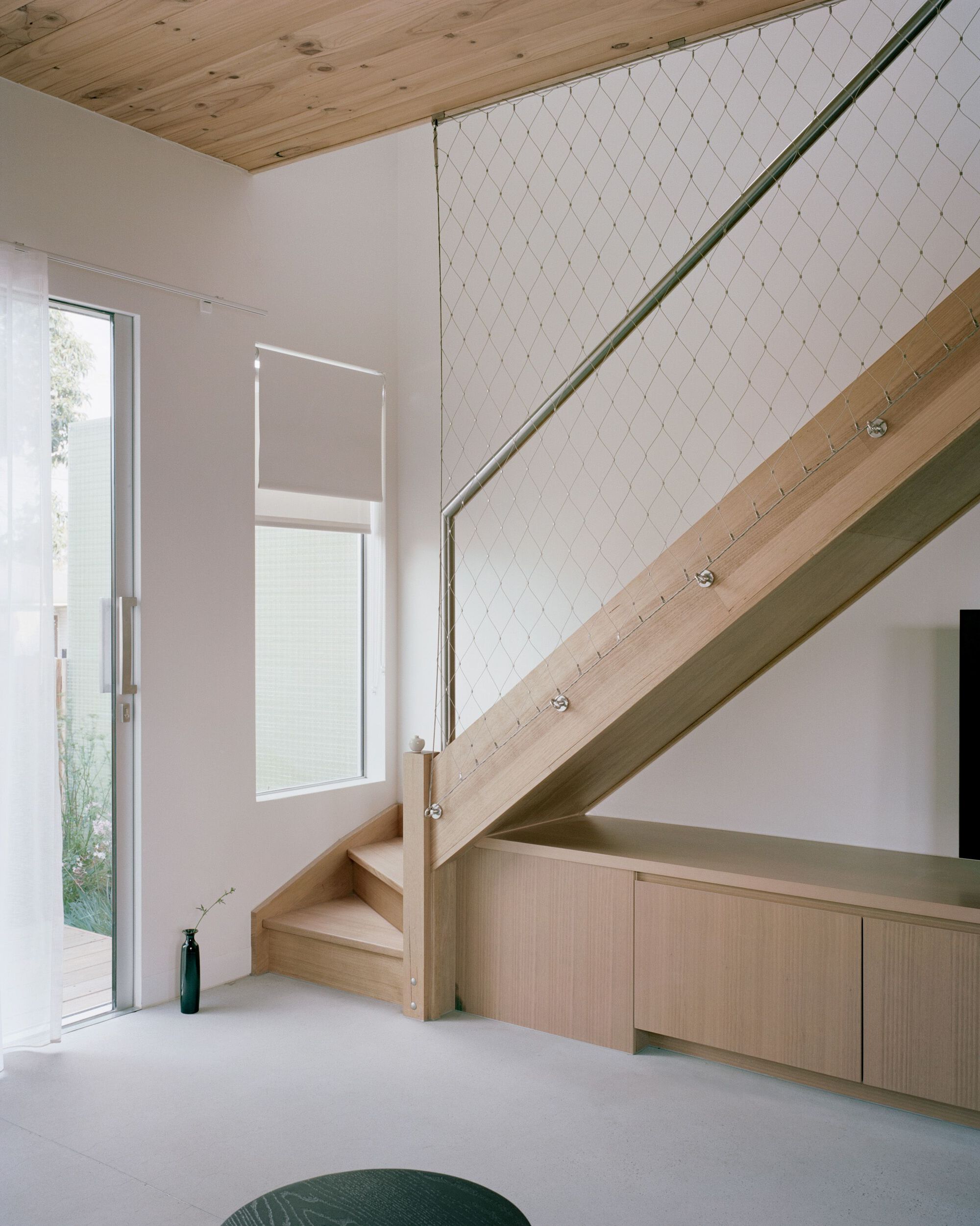 Timber staircase with wire mesh balustrade ascending past built-in cabinetry and glazed door