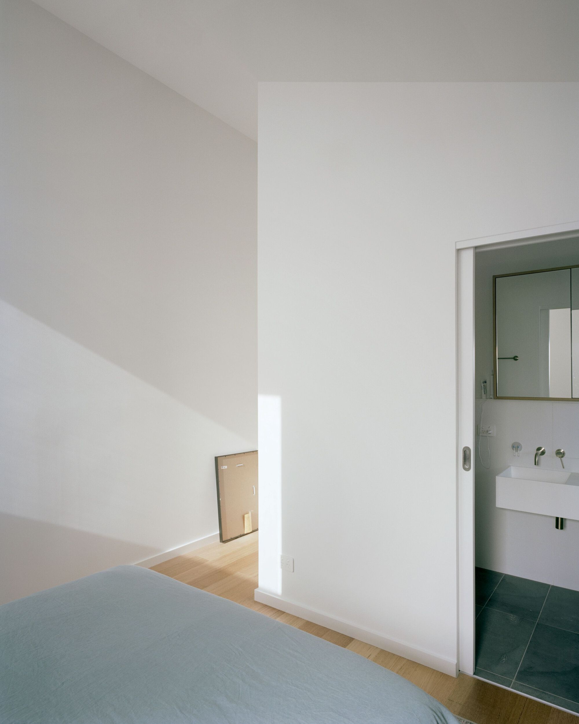 Bedroom with ensuite bathroom door and white partition wall receiving afternoon sunlight from an unseen window