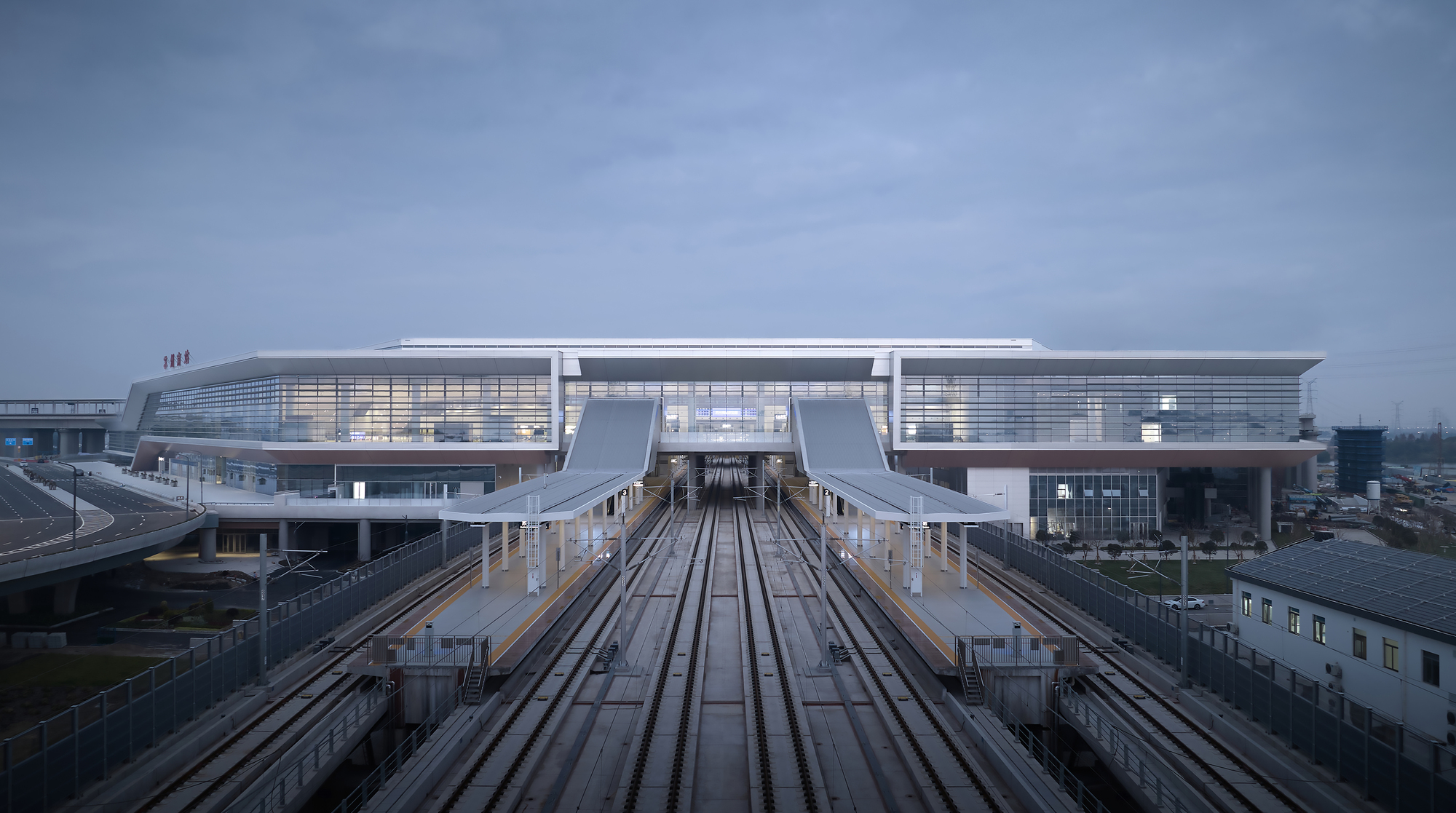 View along elevated rail tracks leading to the illuminated terminal building under overcast skies