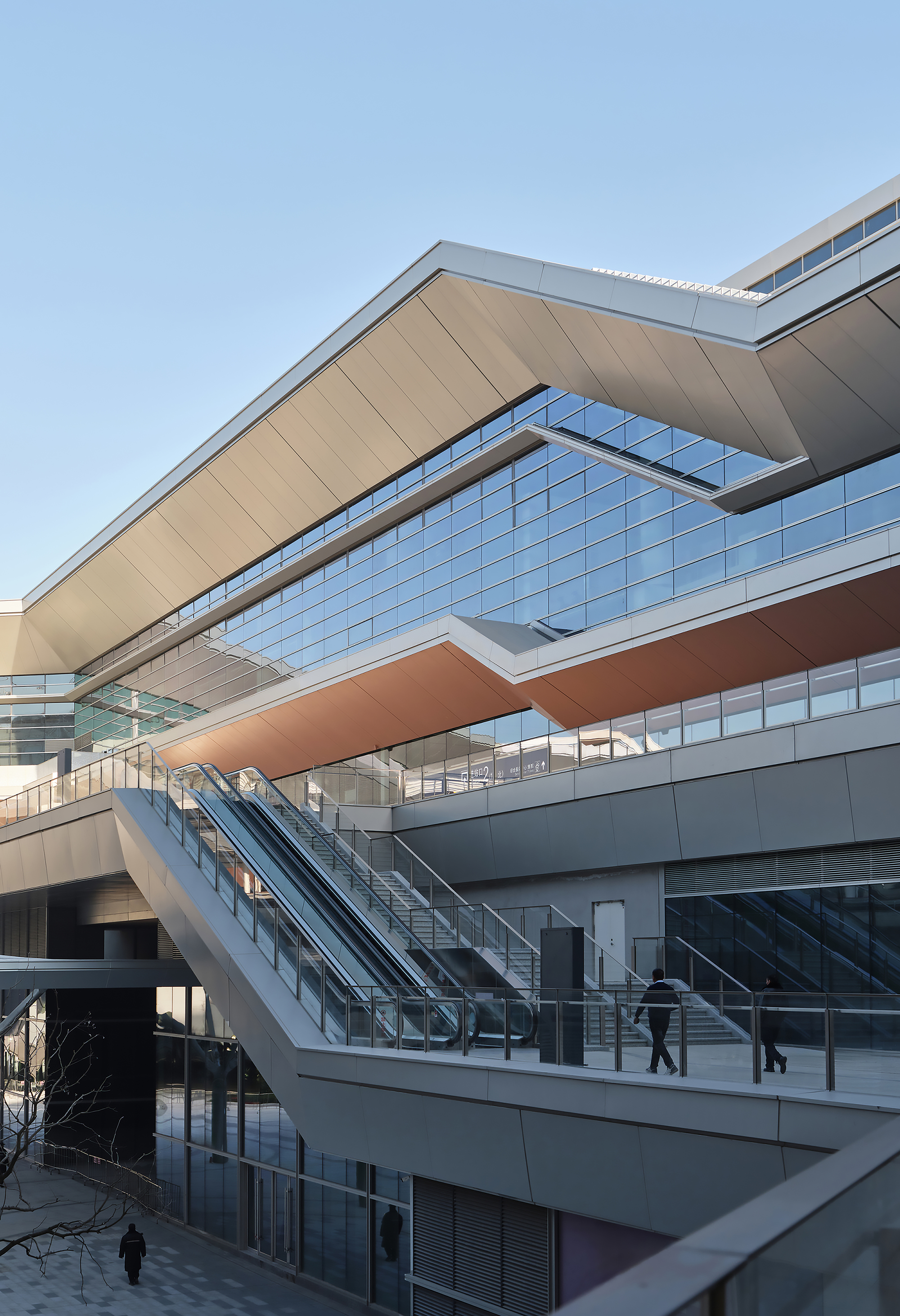 Stacked horizontal volumes with glazed facades and outdoor escalators carrying passengers between levels
