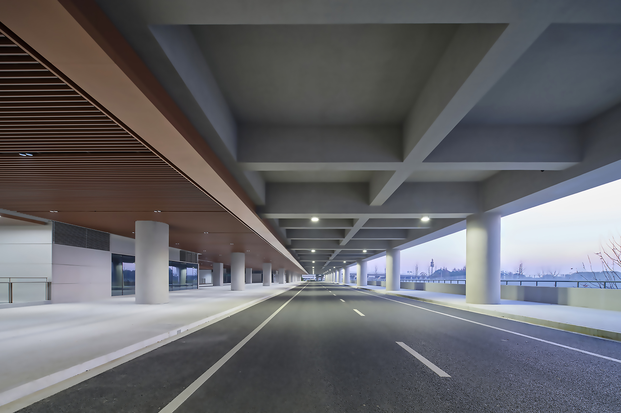 Covered roadway with concrete beams and cylindrical columns framing an open horizon at dusk