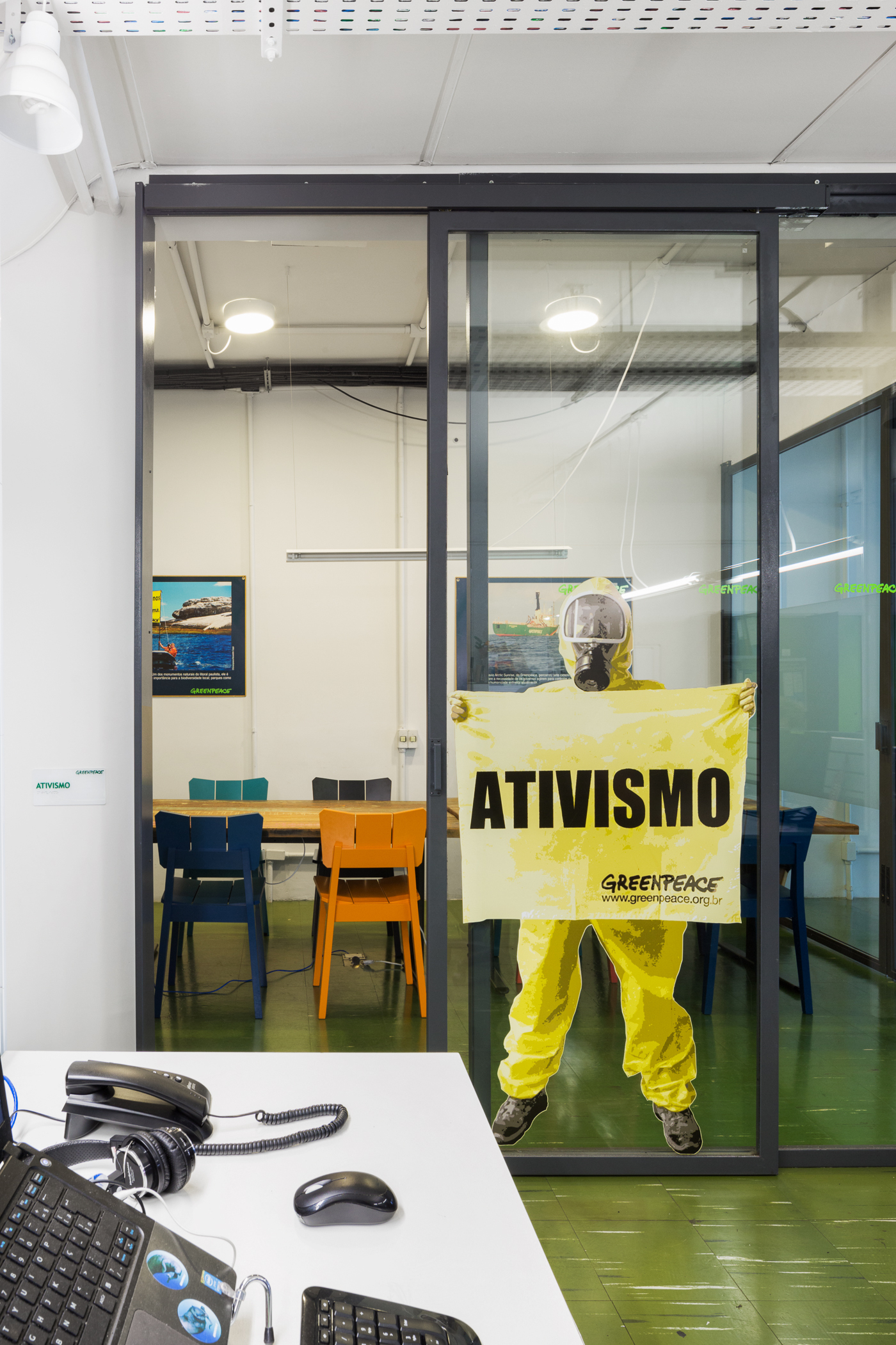 Glass sliding door of a meeting room with a person in a yellow protective suit holding a banner, desk in foreground