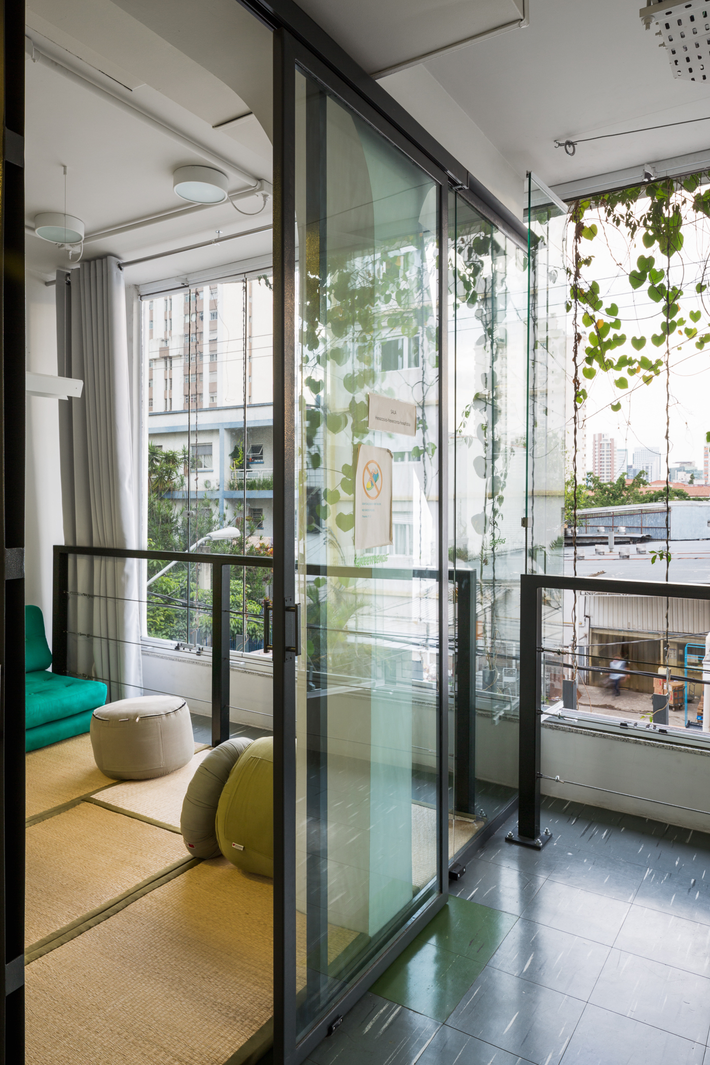 Sliding glass door opening to a tatami lounge with floor cushions, with climbing vines on the window wires in daylight
