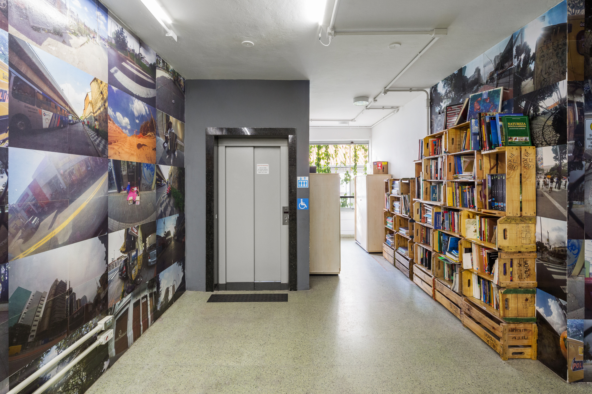 Corridor with a photo-covered wall beside the elevator and a shelf of timber crates holding books