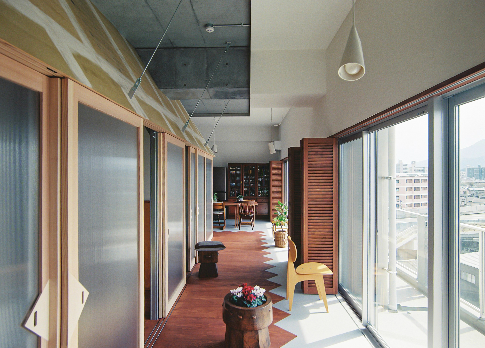 Long corridor with translucent sliding panels, exposed concrete ceiling and terracotta flooring under daylight