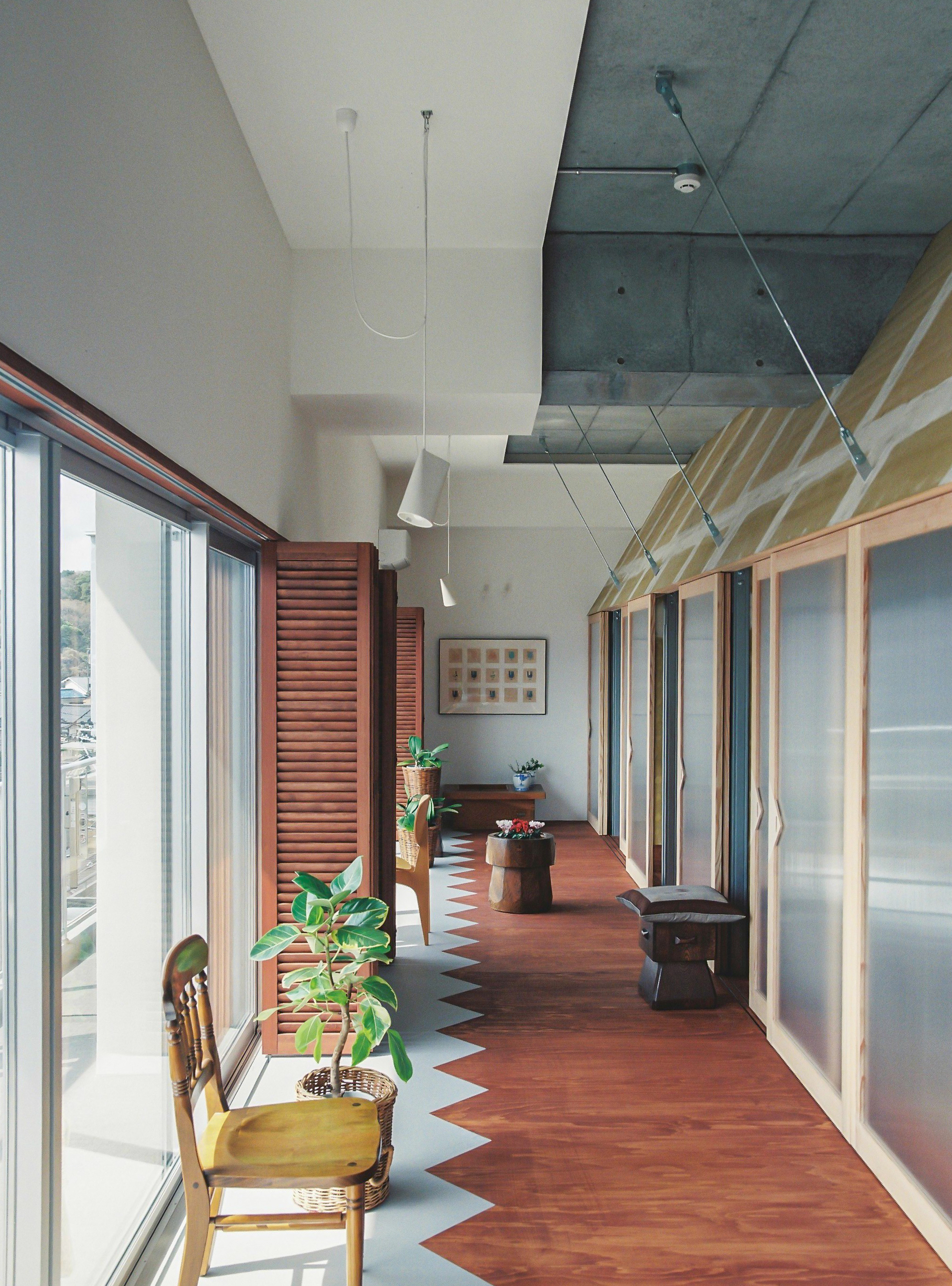 Corridor with zigzag terracotta and white floor tile pattern alongside louvered timber shutters and translucent panels