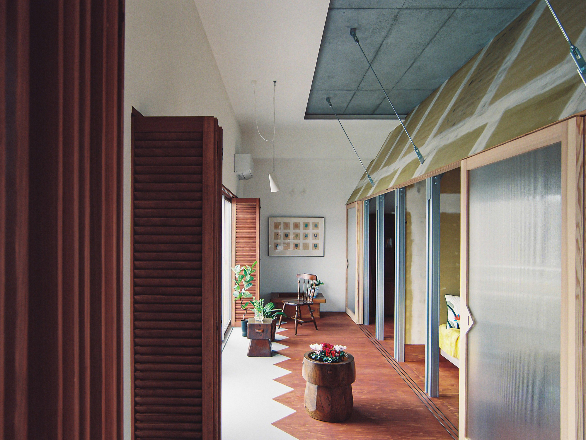 Interior passage showing exposed concrete ceiling soffit, pendant lights, and potted plants on patterned floor