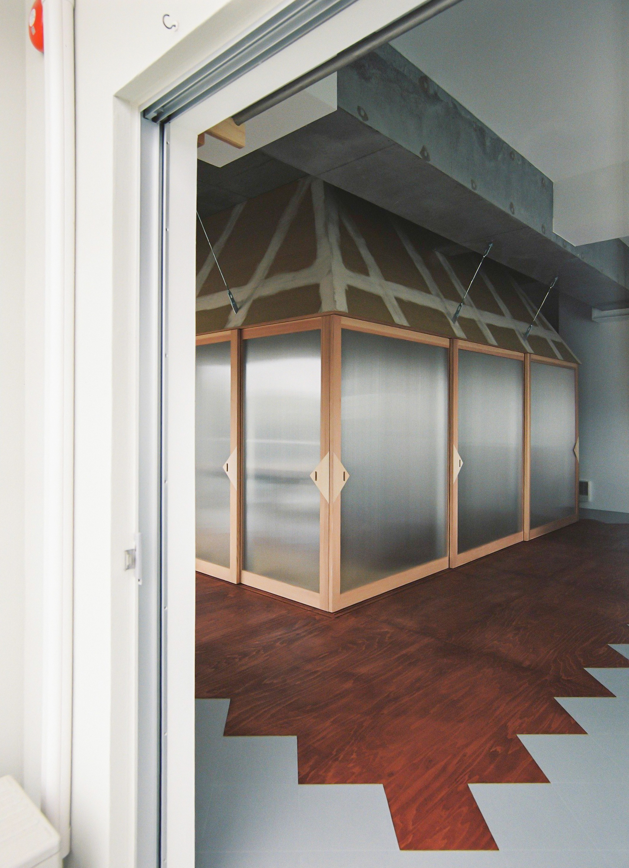 Timber-framed translucent partition wall with exposed truss structure visible above and chevron floor pattern